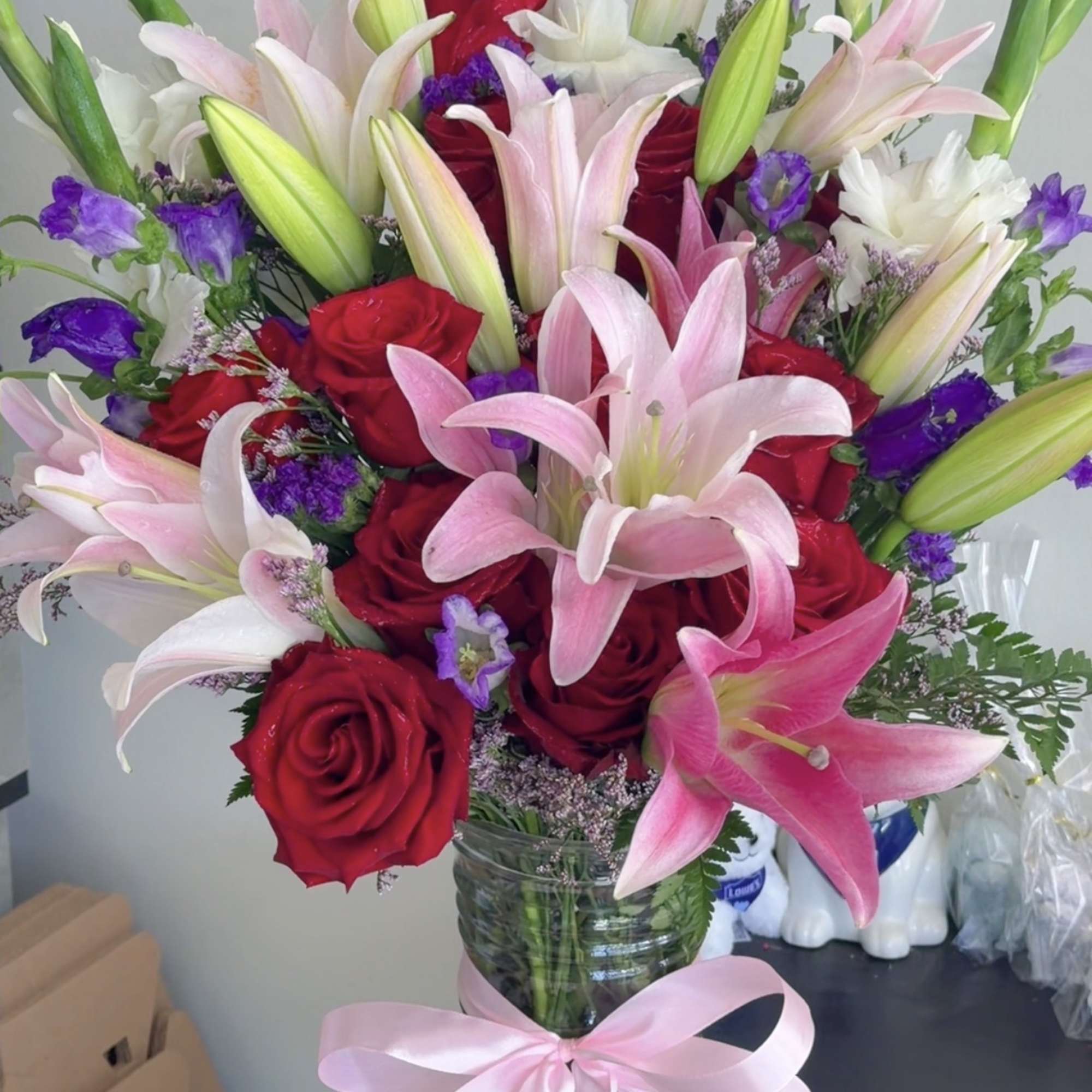Bouquet of red roses and pink lilies in a glass vase with a pink ribbon.