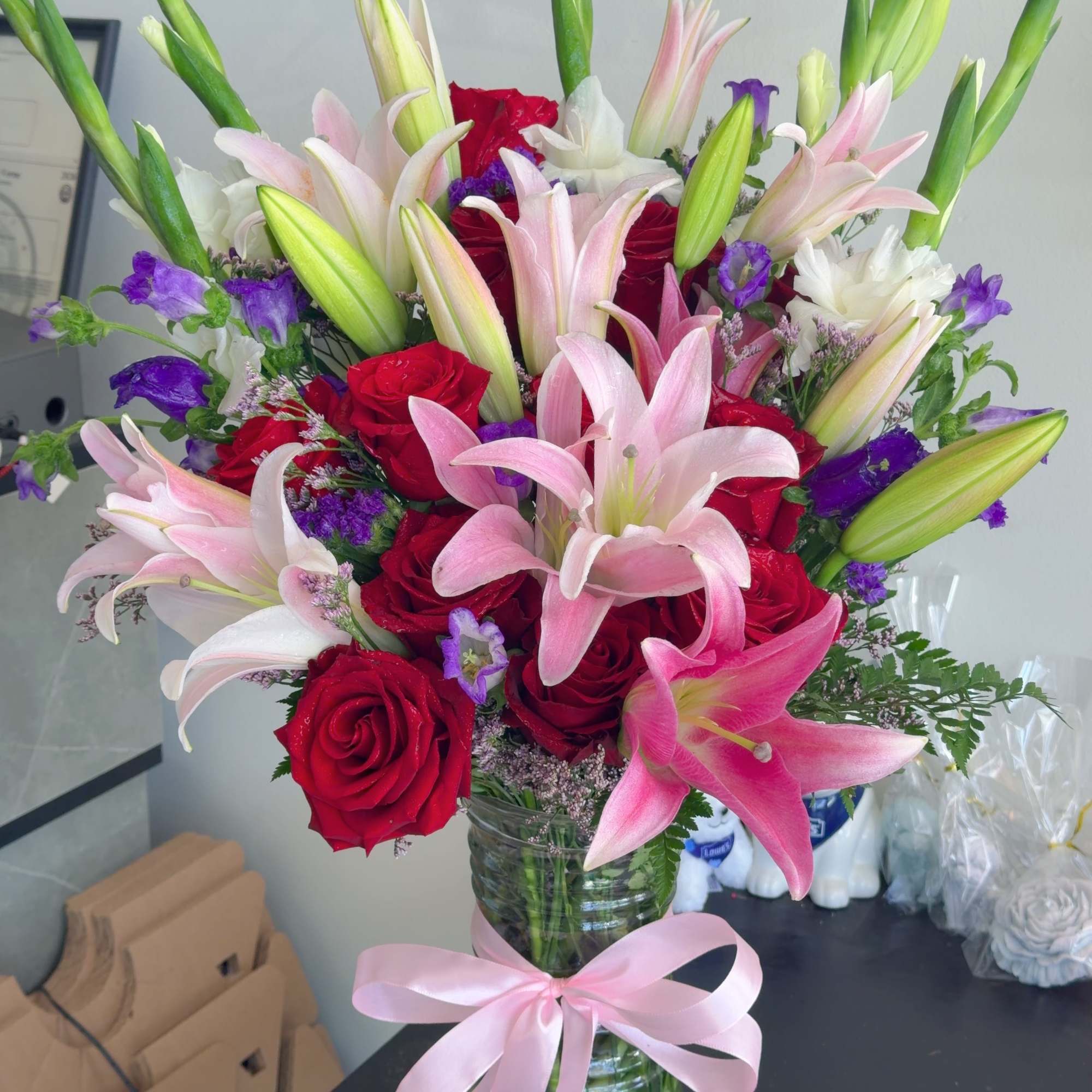 Bouquet of pink lilies and red roses in a glass vase with a pink ribbon
