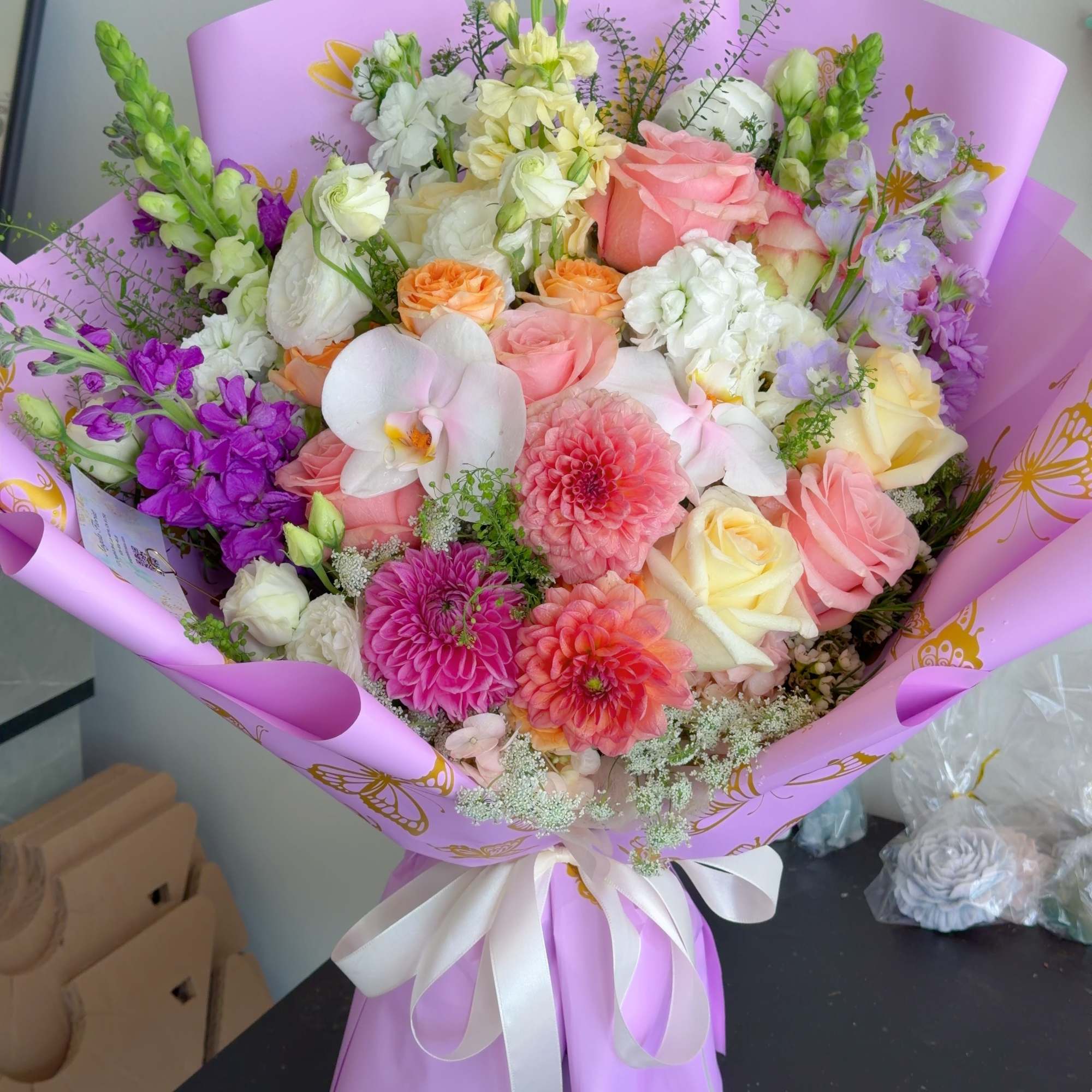 Mixed bouquet of pink, white, yellow, and purple flowers wrapped in lavender paper