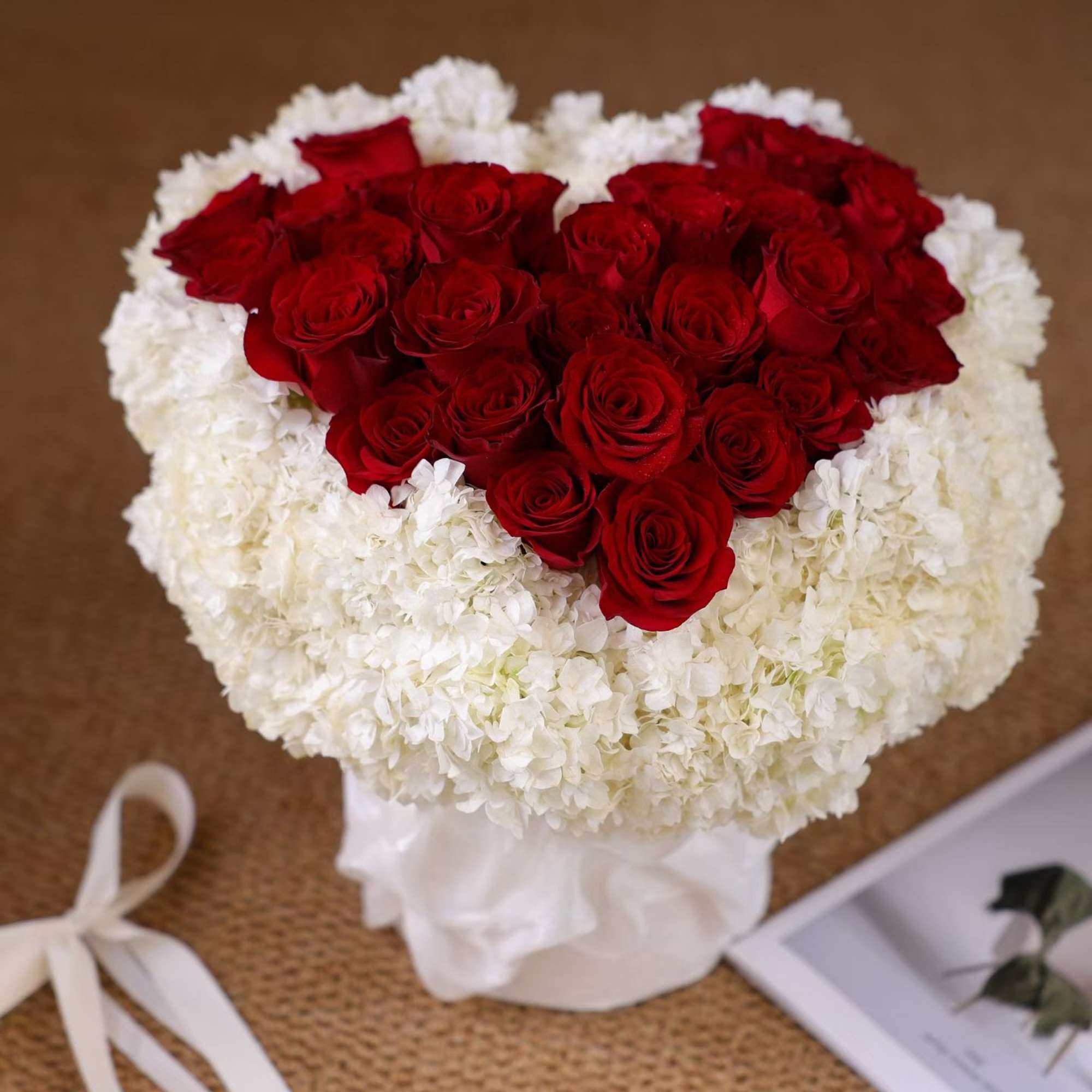 Heart-shaped bouquet of red roses surrounded by white hydrangeas