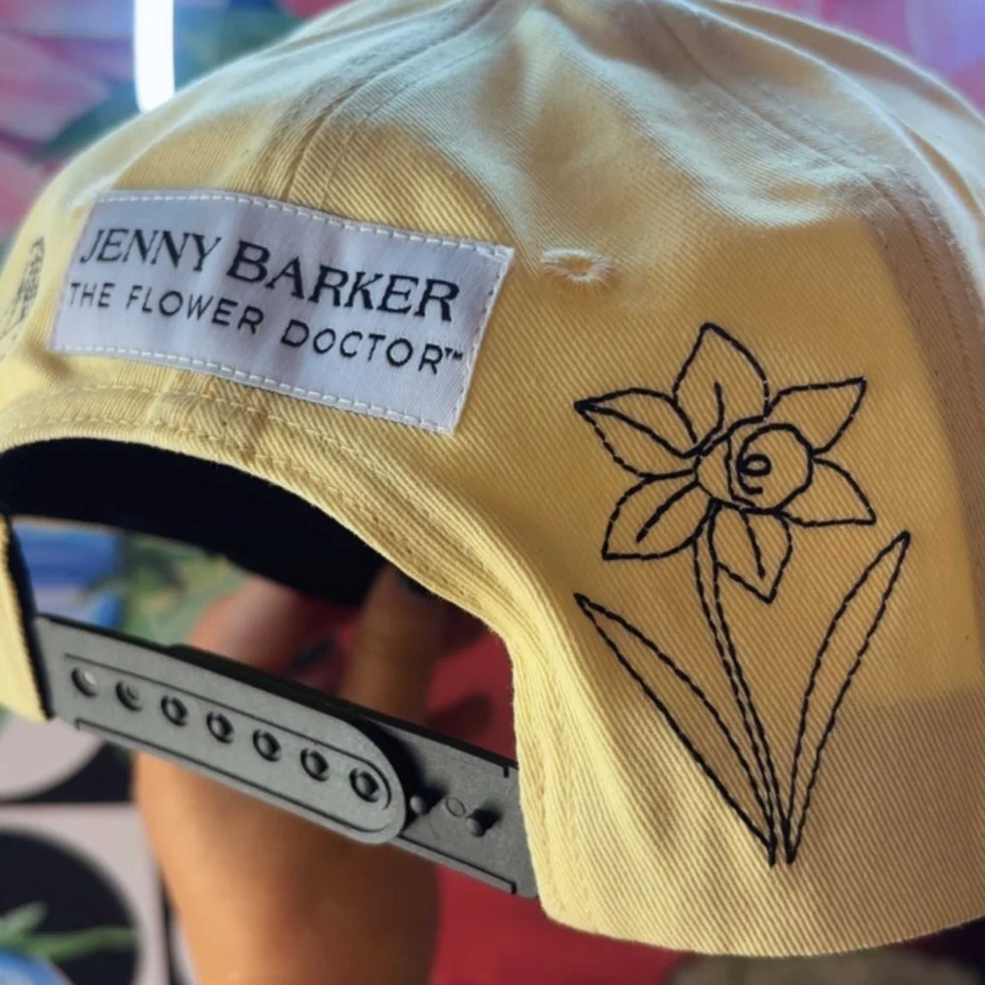 Yellow cap with a flower logo and Jenny Barker patch