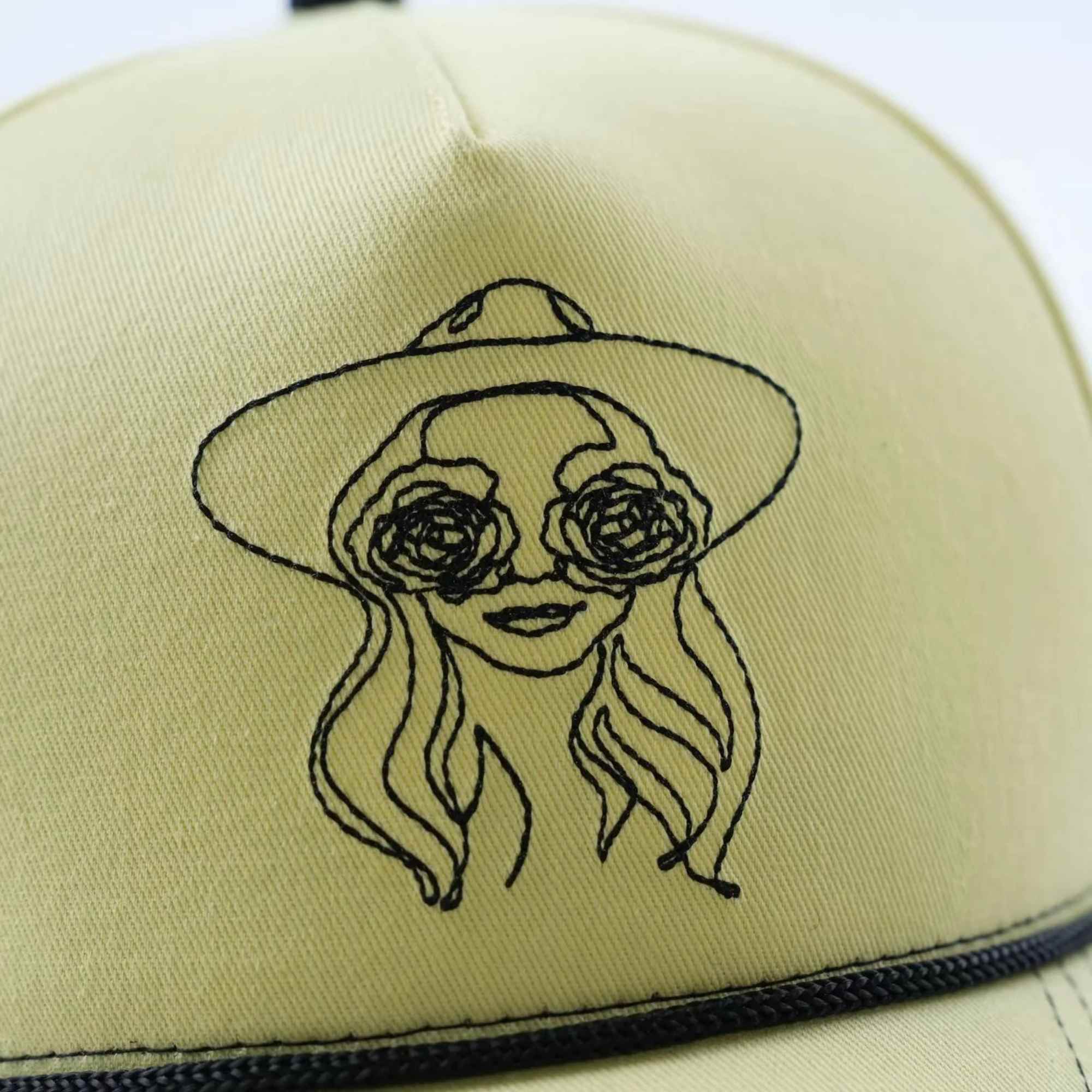 Yellow cap with a black line drawing of a woman in a hat and rose-shaped glasses