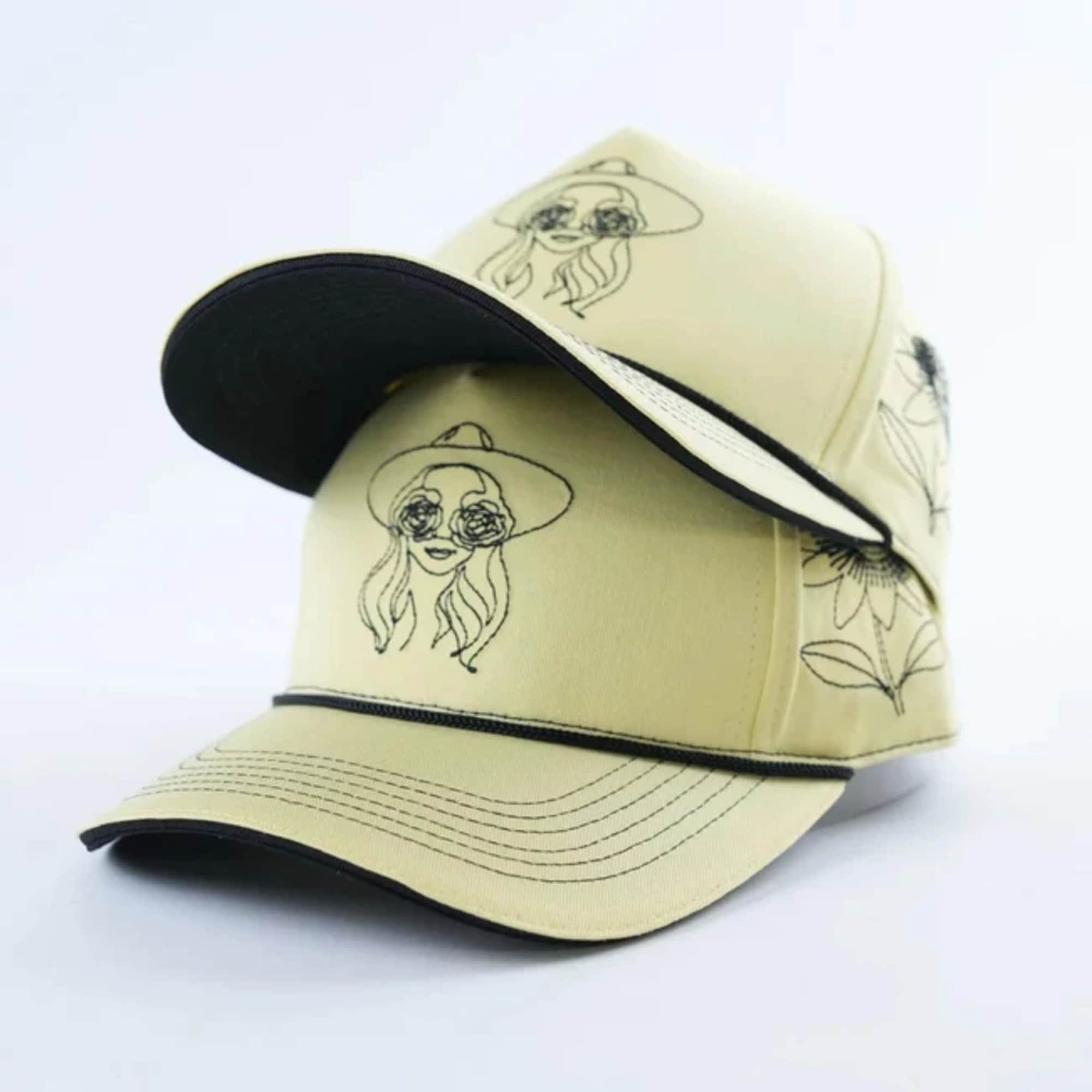 Two beige baseball caps with black line drawings and black brims