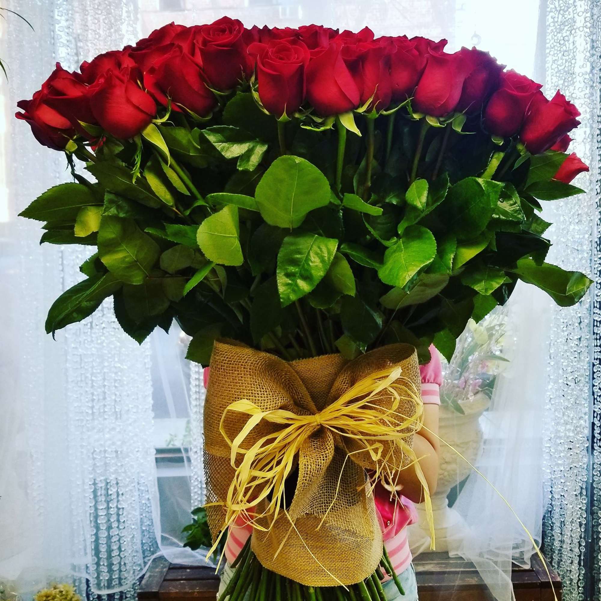 Large bouquet of red roses wrapped in burlap with a yellow ribbon