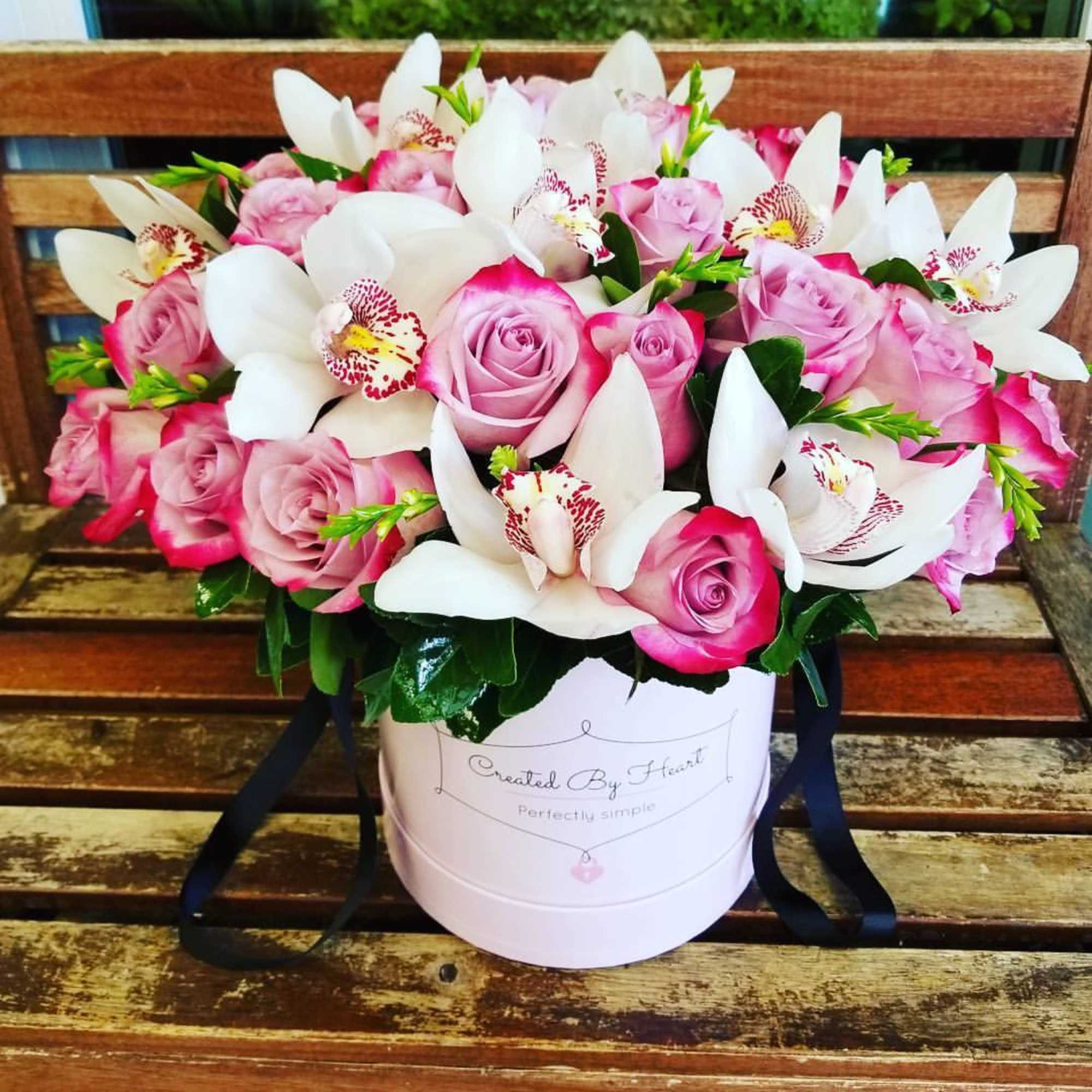 Pink roses and white orchids arranged in a round hat box