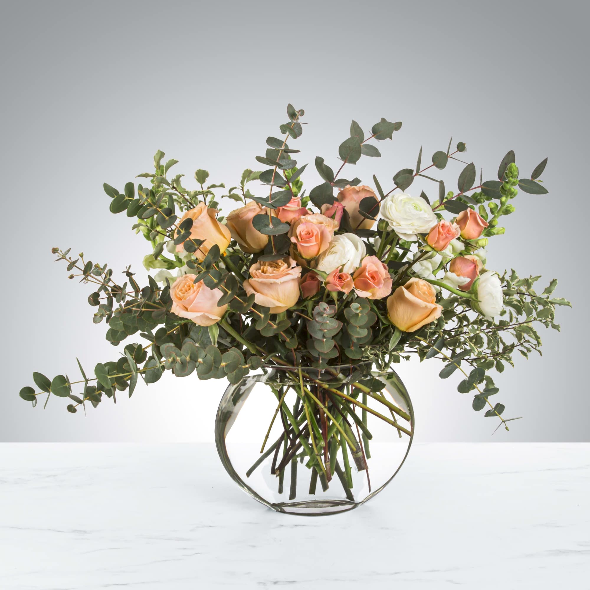 Peach and white roses in a round glass vase with eucalyptus