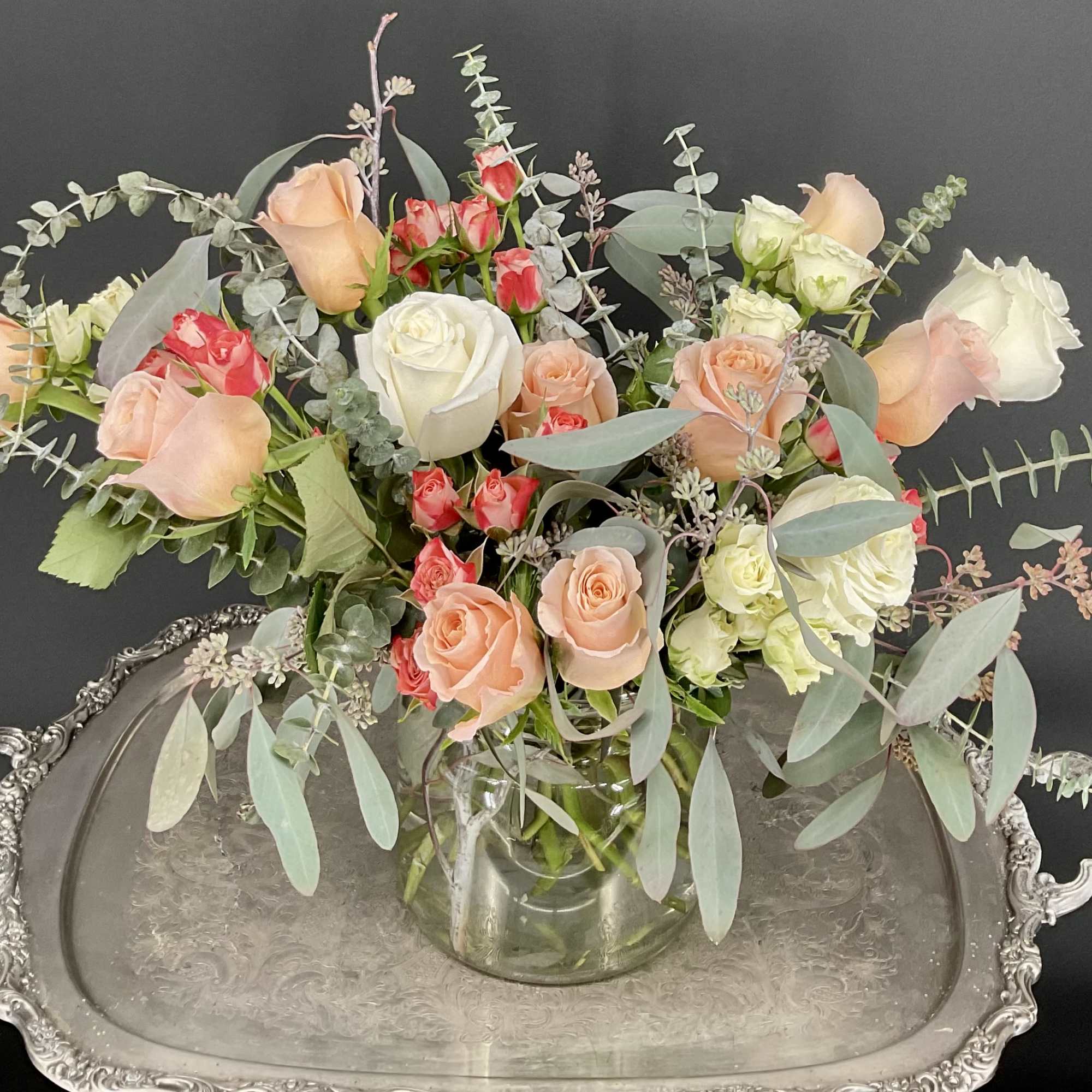 Mixed roses in a clear glass vase with airy eucalyptus on a silver tray