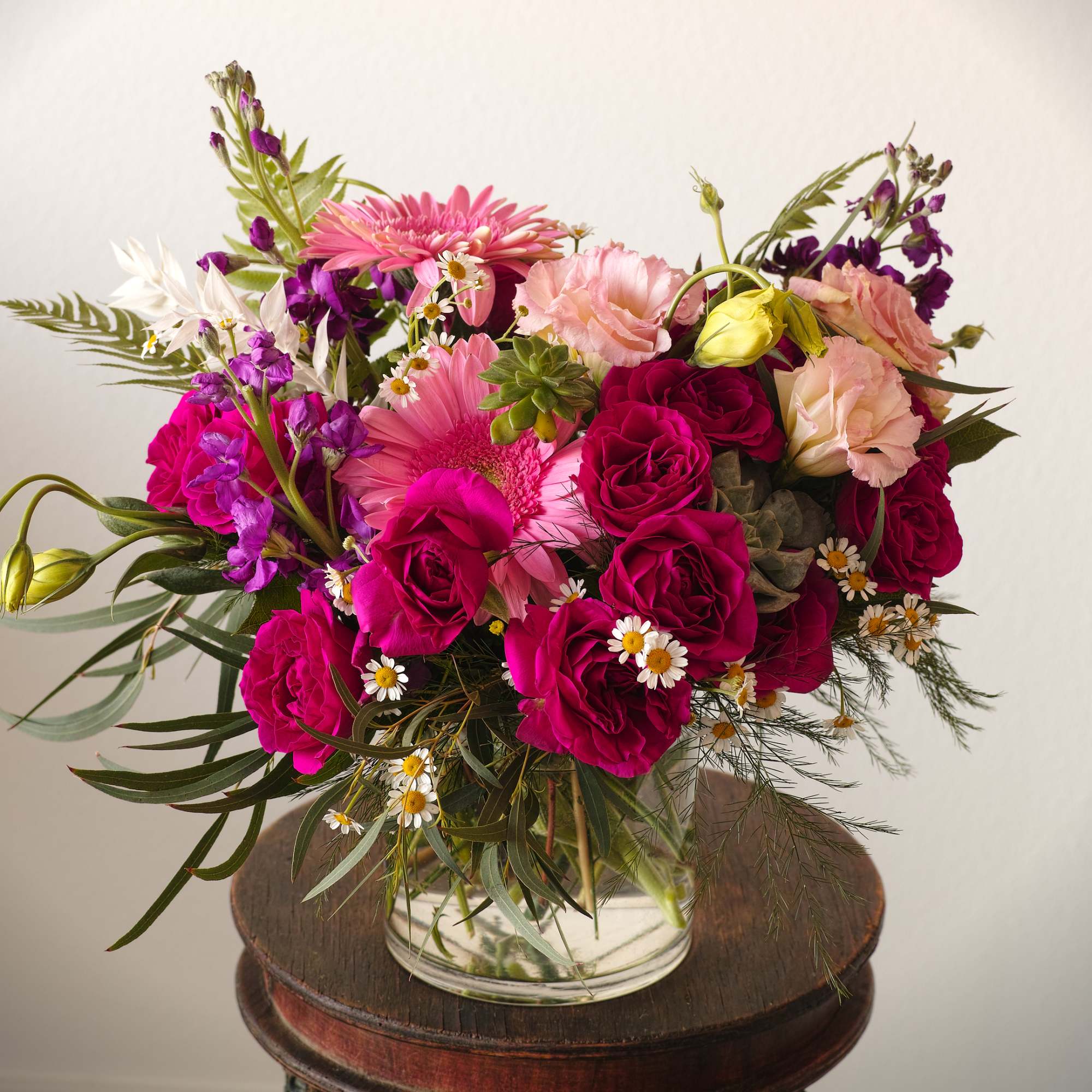 Pink and magenta bouquet with roses, gerbera daisies, and small white daisies in a glass vase