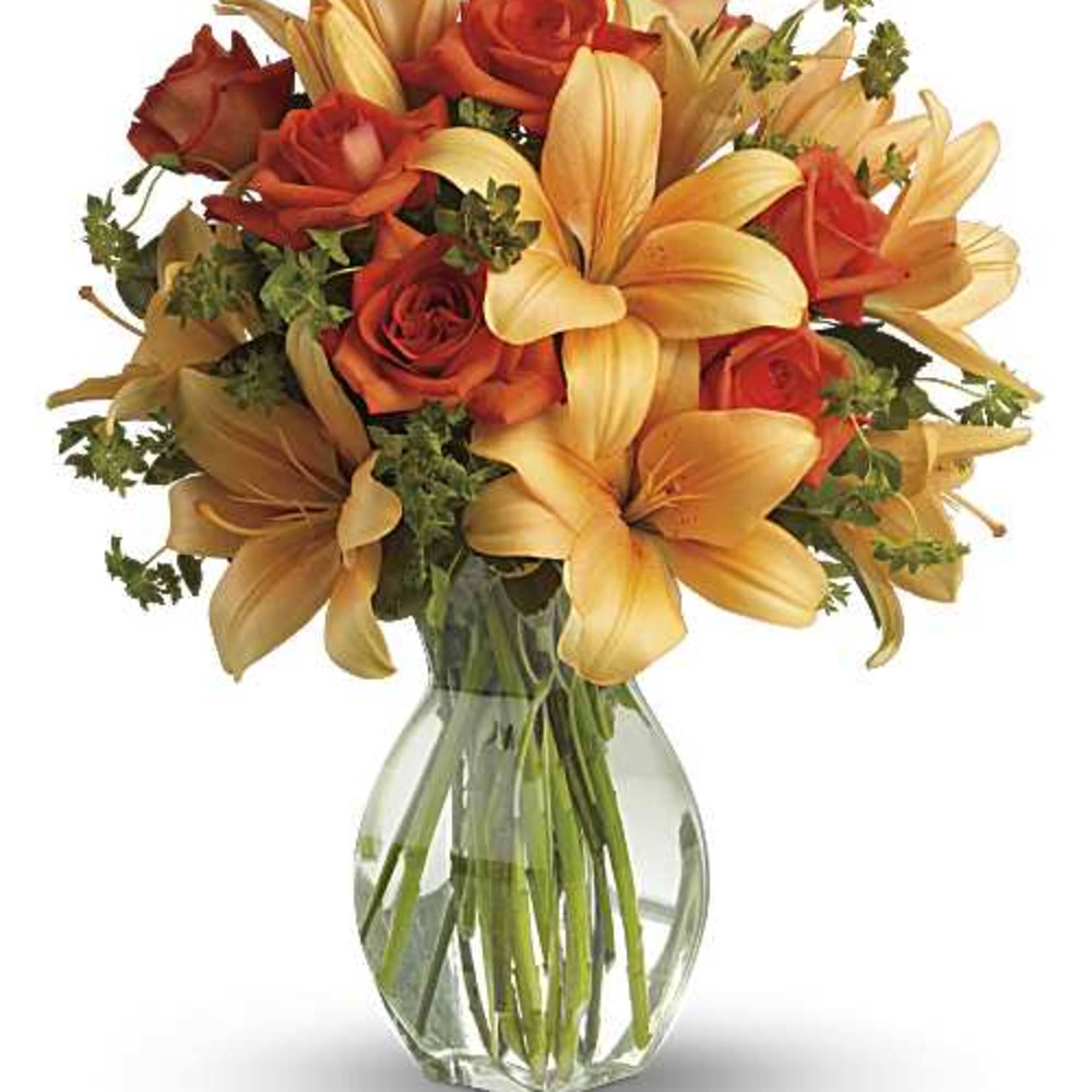 Orange roses and peach lilies arranged in a clear glass vase