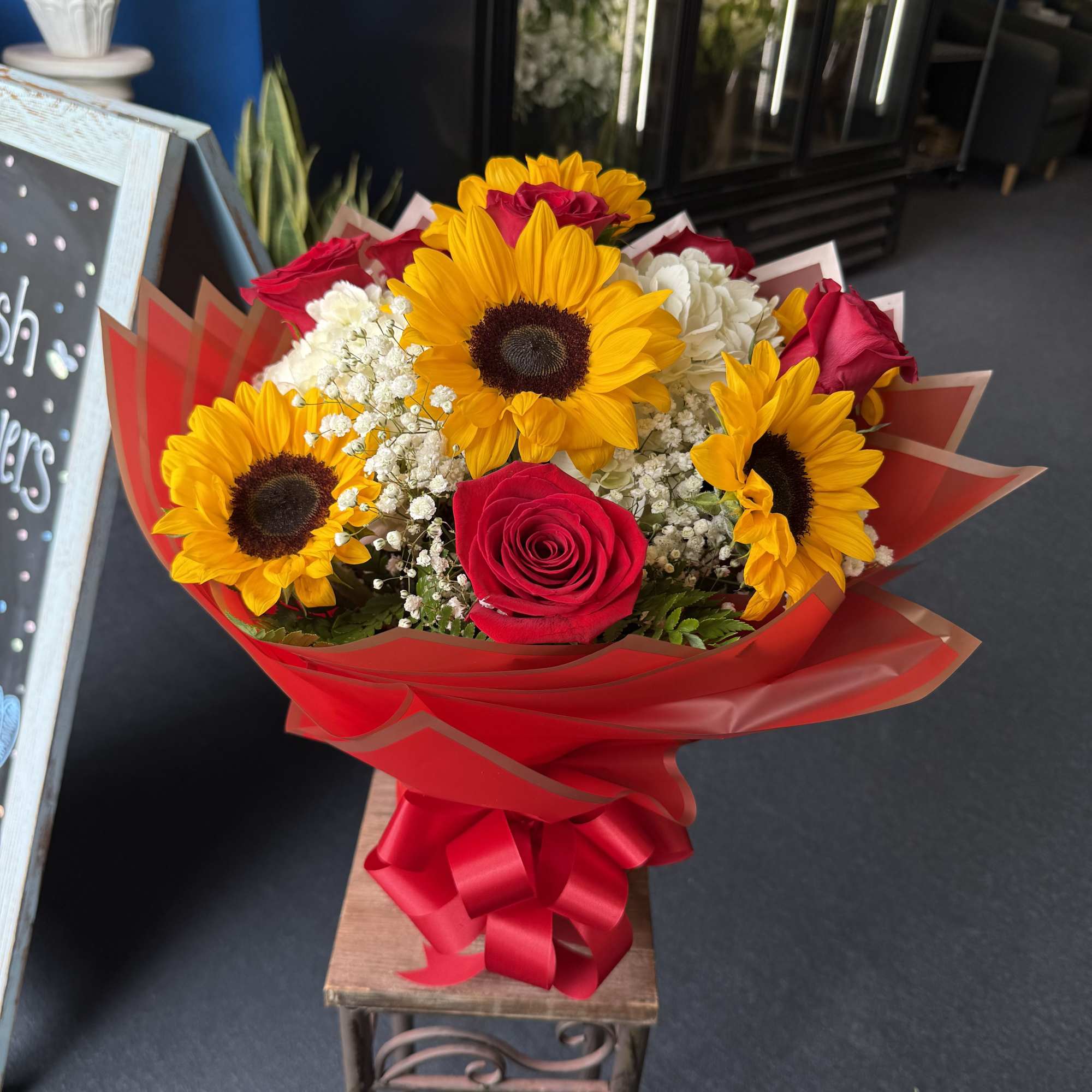 Bright sunflowers, vivid red roses and white accents wrapped in bold red