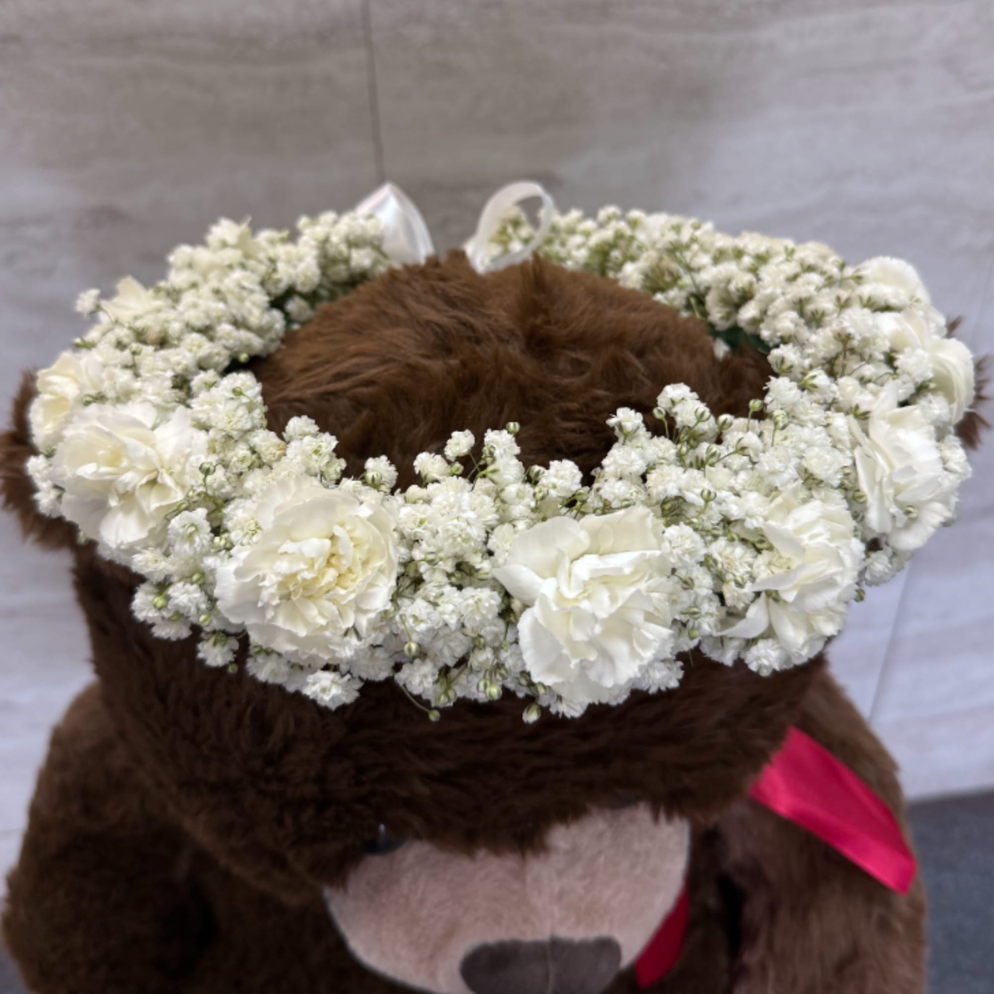 White carnation halo with baby's breath around a brown plush bear, finished