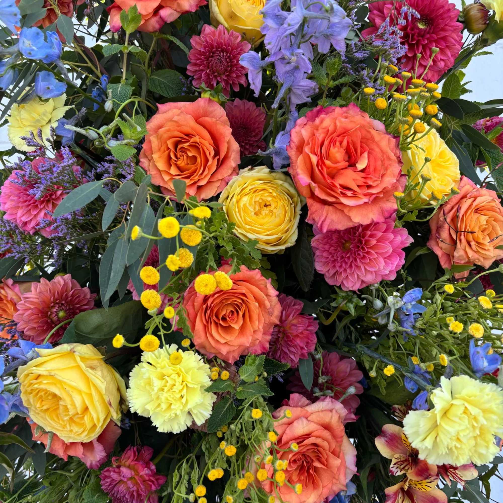 Mixed bouquet with orange and yellow roses, pink blooms, and blue flowers