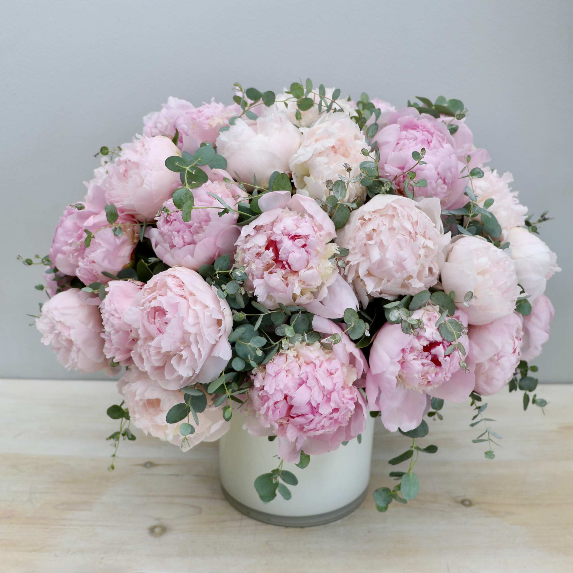 Round arrangement of light pink peonies with eucalyptus in a white cylinder vase