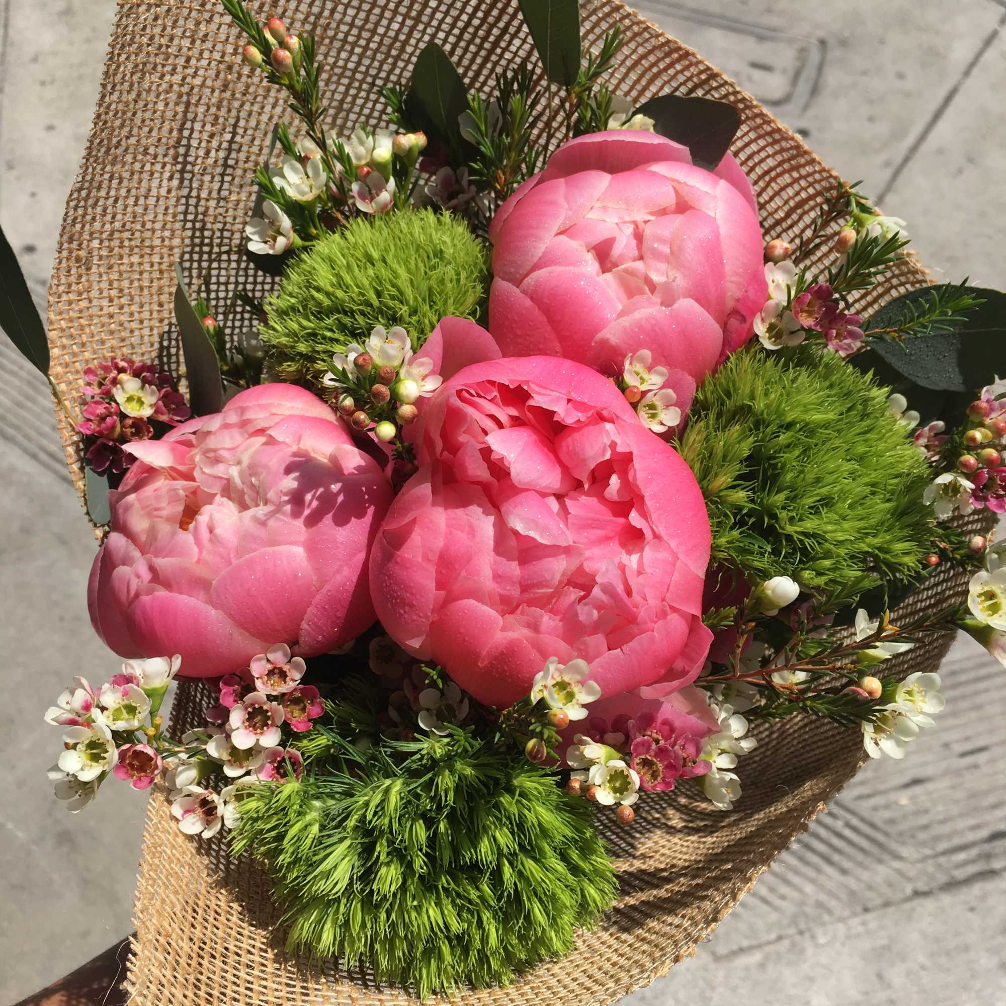 Pink peony bouquet with small white blossoms wrapped in burlap