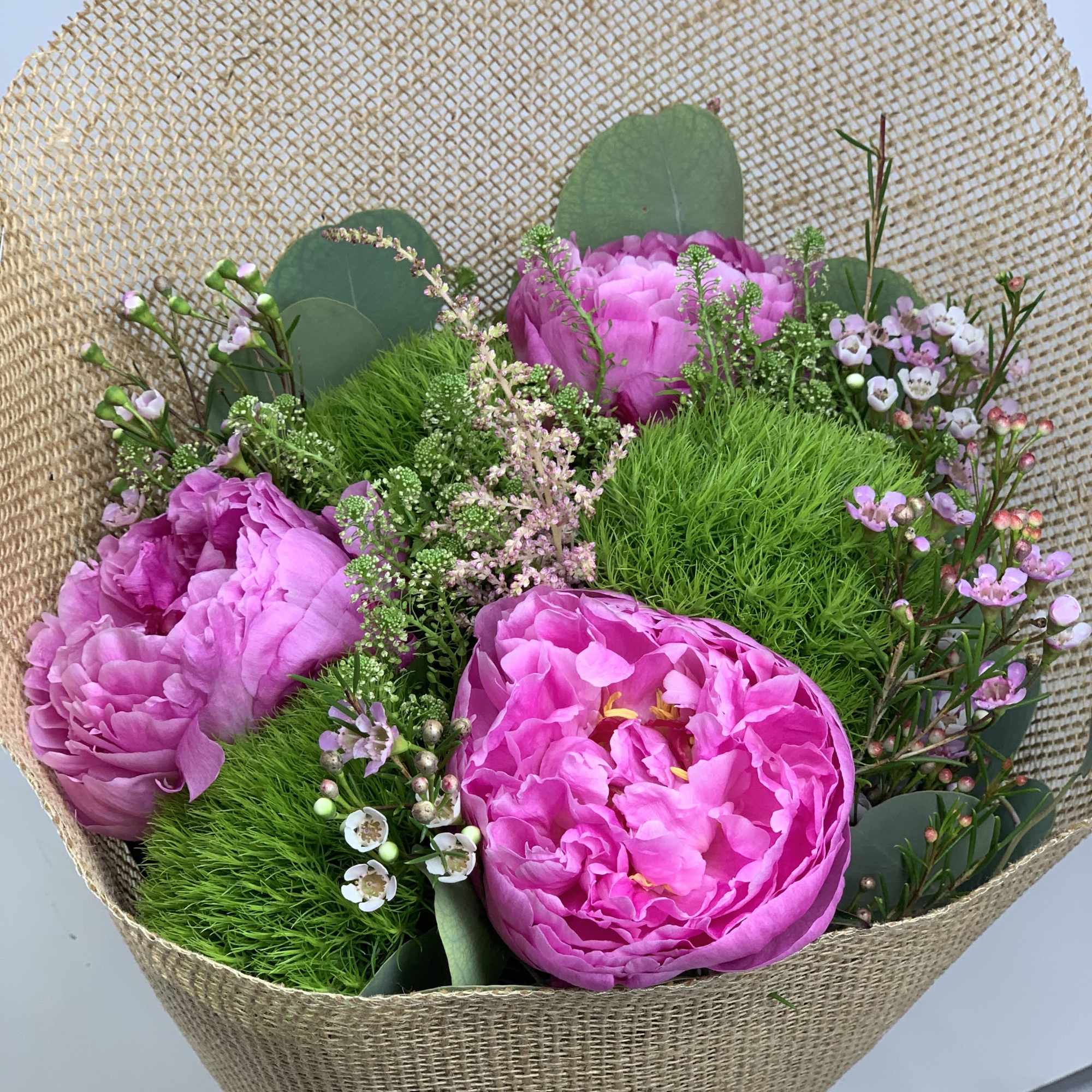 Pink peonies in a burlap-wrapped bouquet with small filler flowers
