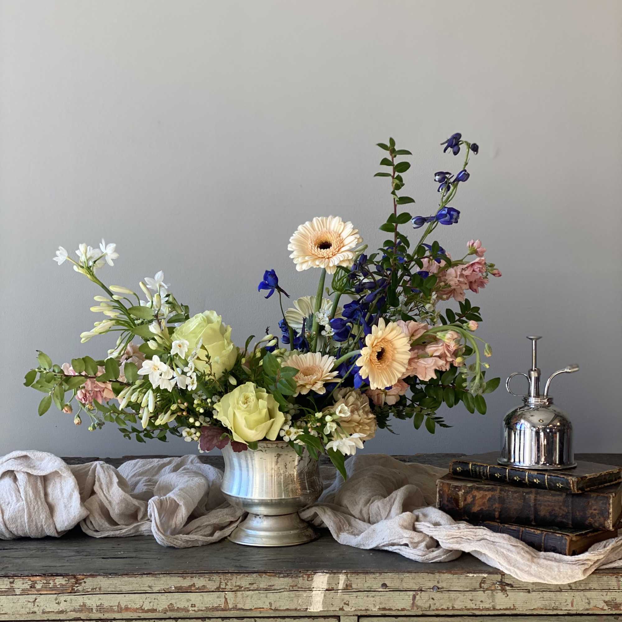 Mixed flower arrangement in a silver vase with peach, white, and blue blooms
