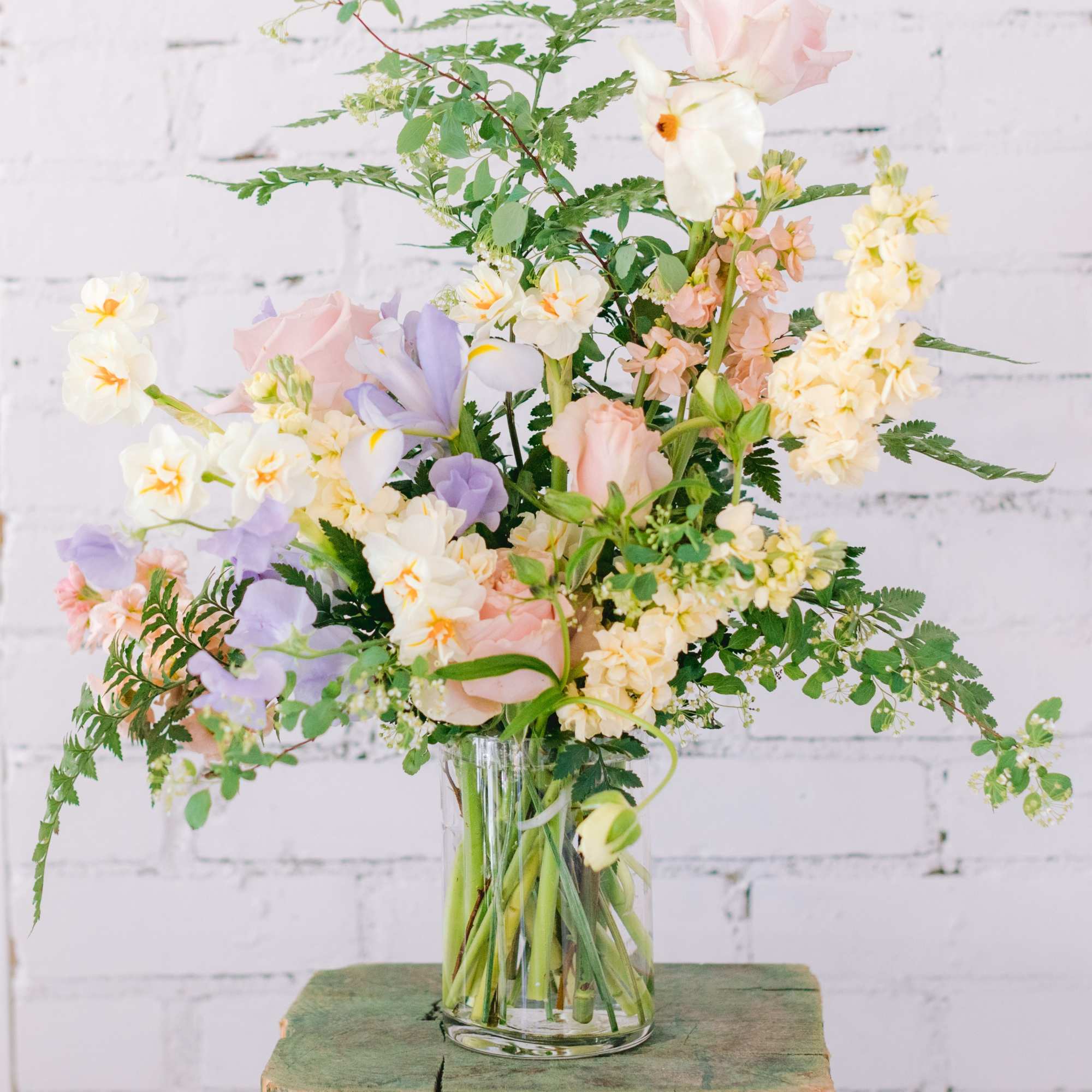 Loose pastel arrangement of roses, daffodils, stock, and sweet peas in a clear glass vase