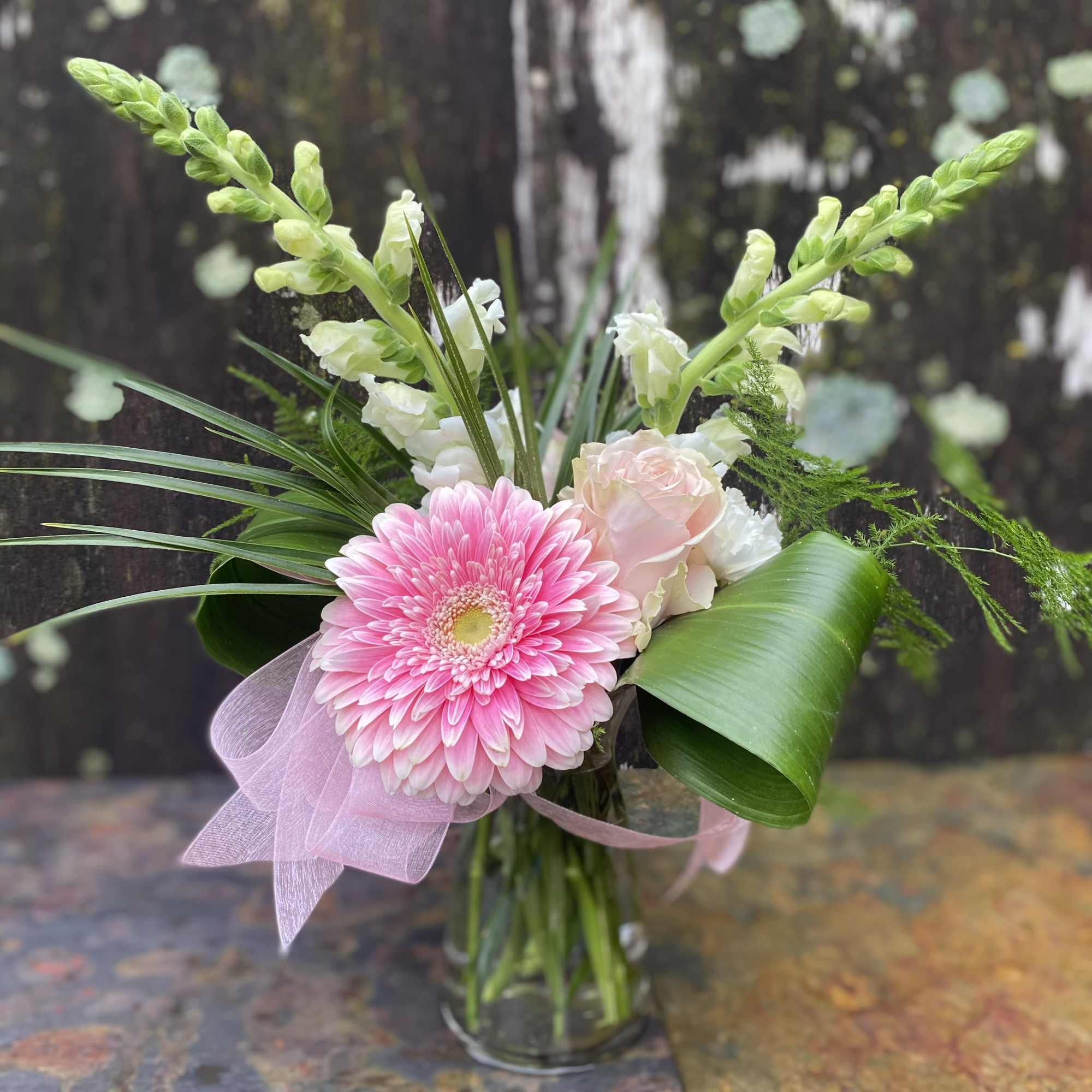 Pink gerbera bouquet in a glass vase with white blooms and ribbon