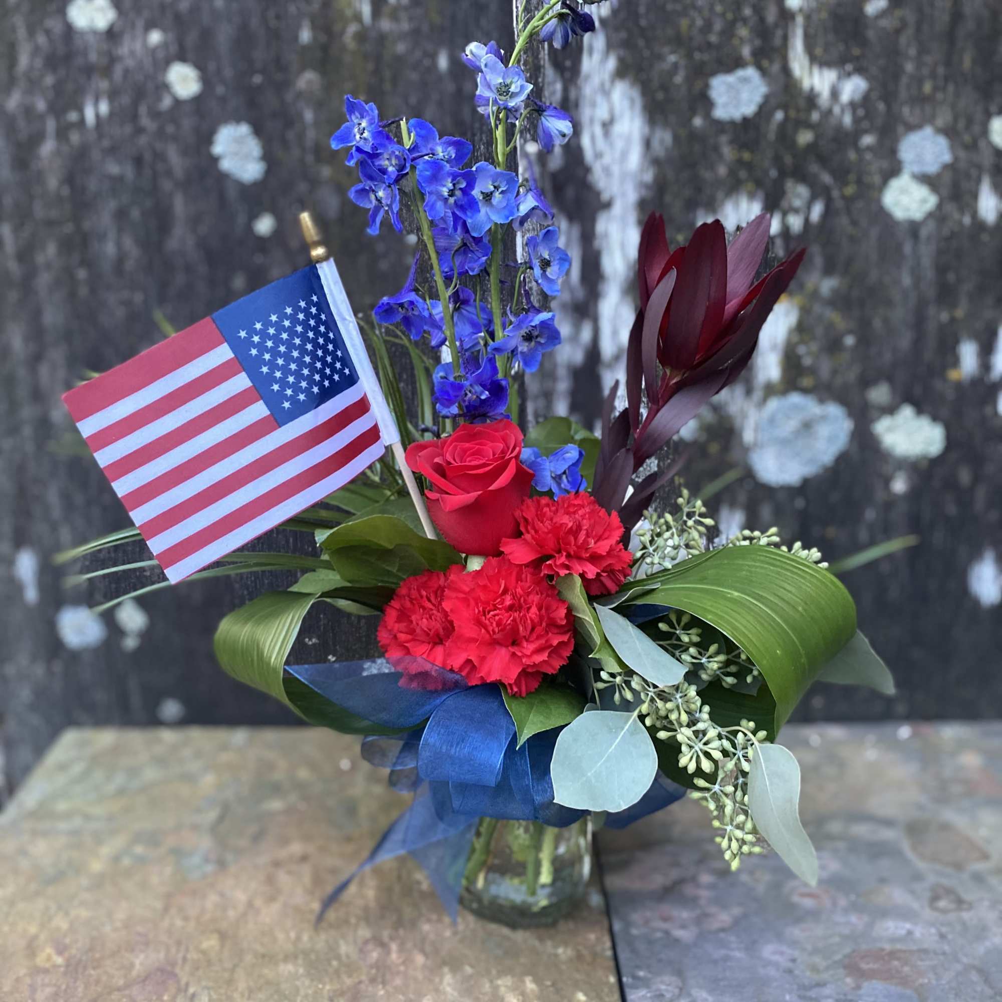 Red and blue floral arrangement in a glass vase with an American flag