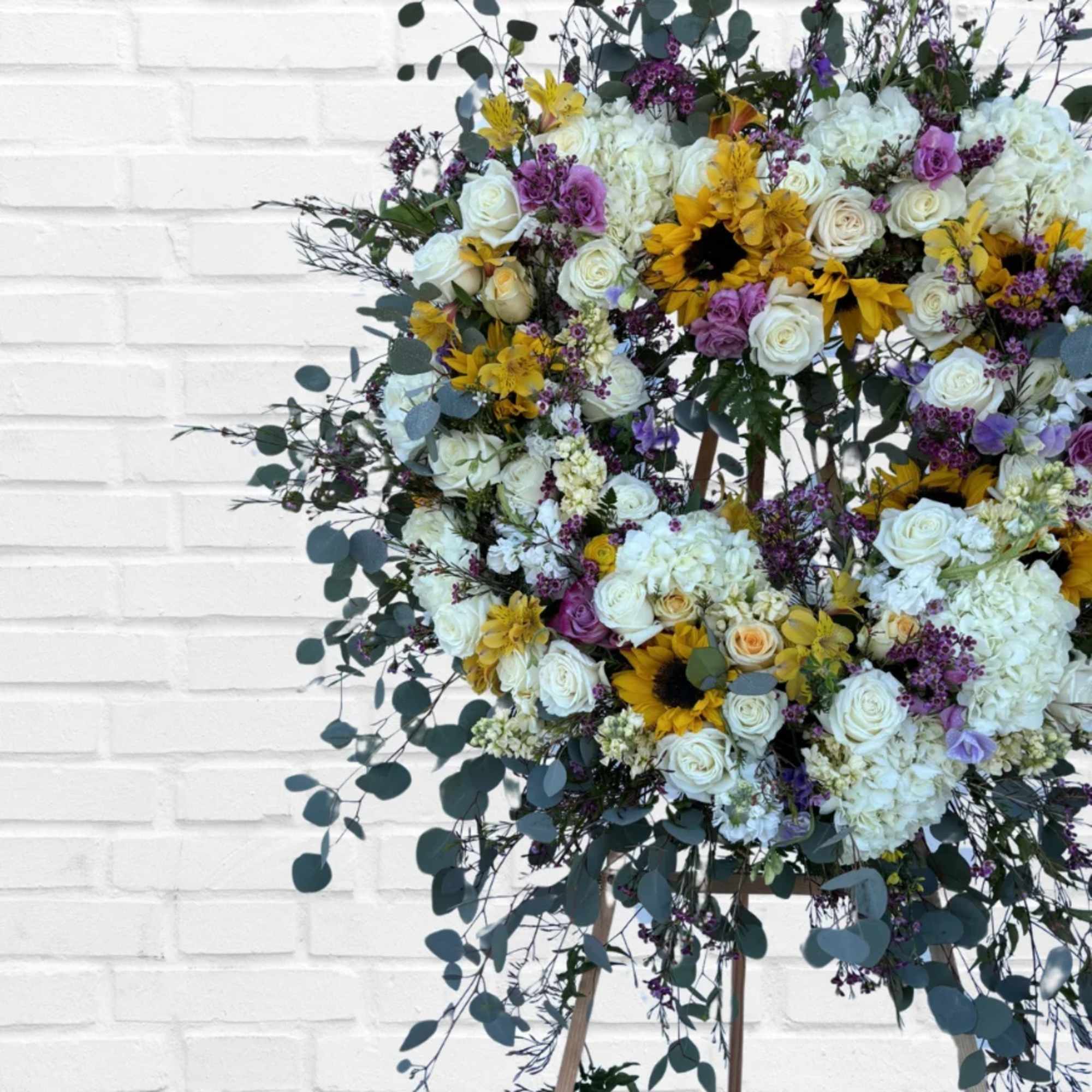 Large floral wreath with white roses, sunflowers, and purple blooms