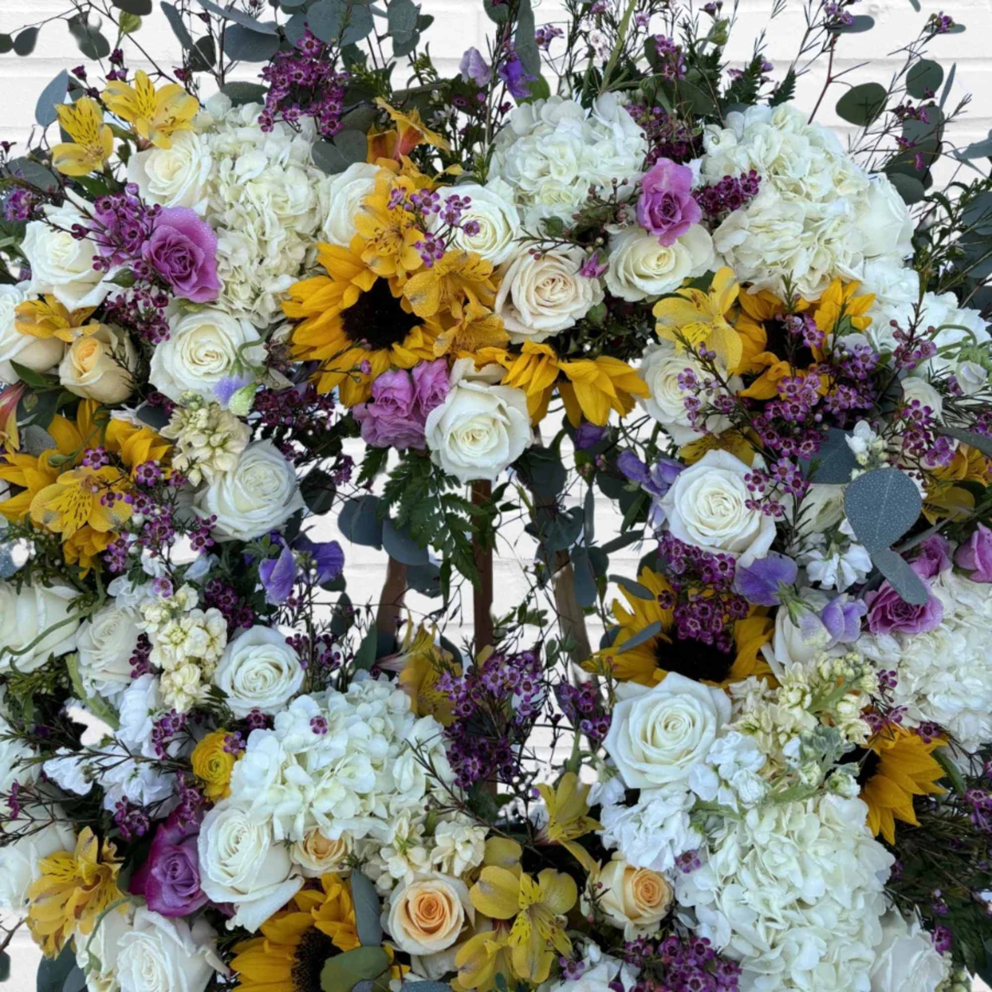 Large floral wreath with white roses, hydrangeas, sunflowers, and purple accents