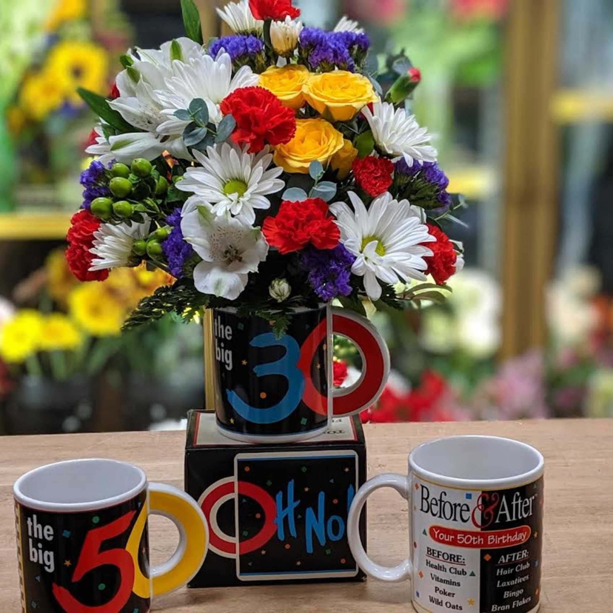 Colorful flower arrangement in a novelty mug with two birthday mugs in front