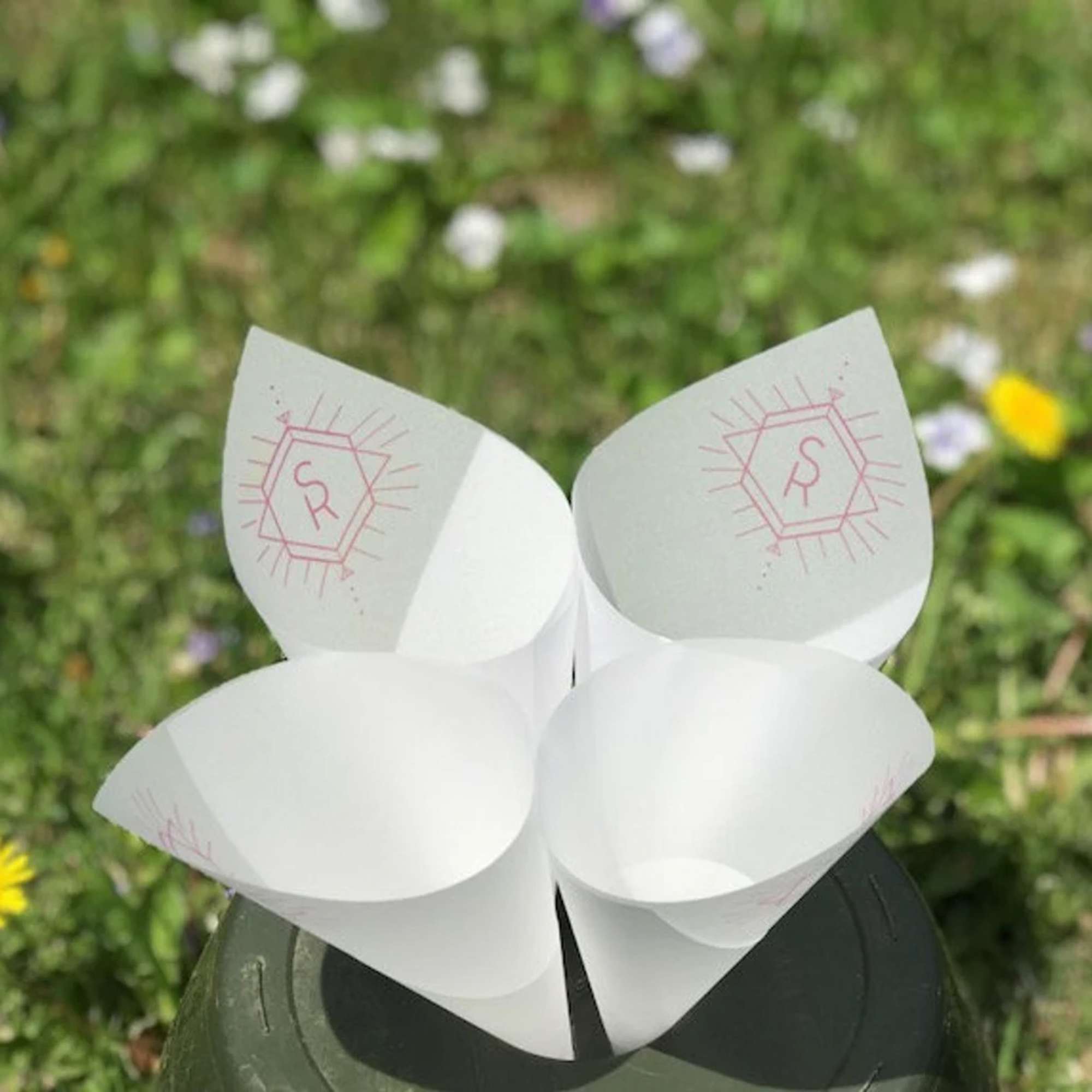 Four white paper cone holders with pink monogram marks on a dark base
