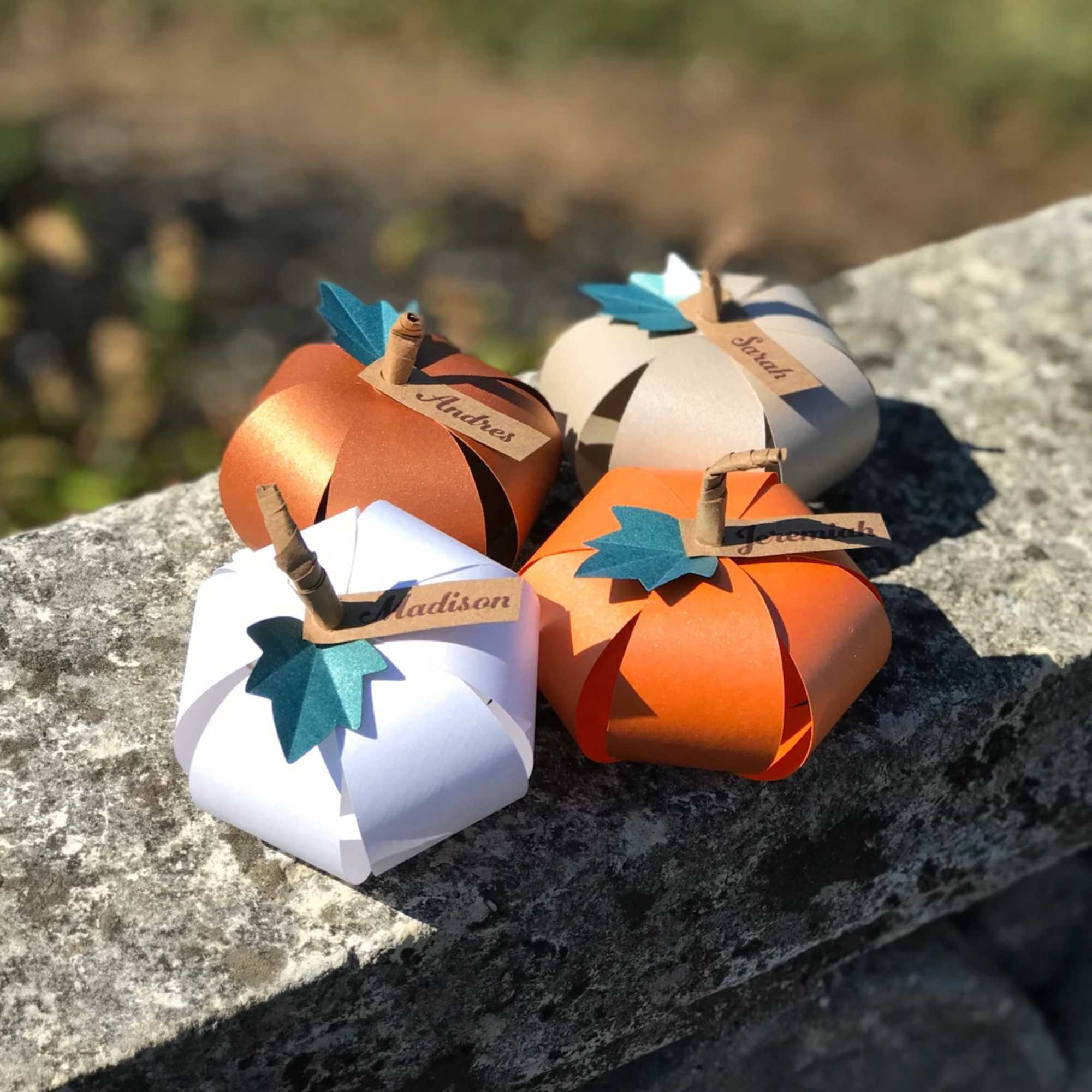 Four paper pumpkins with name tags arranged on a stone surface