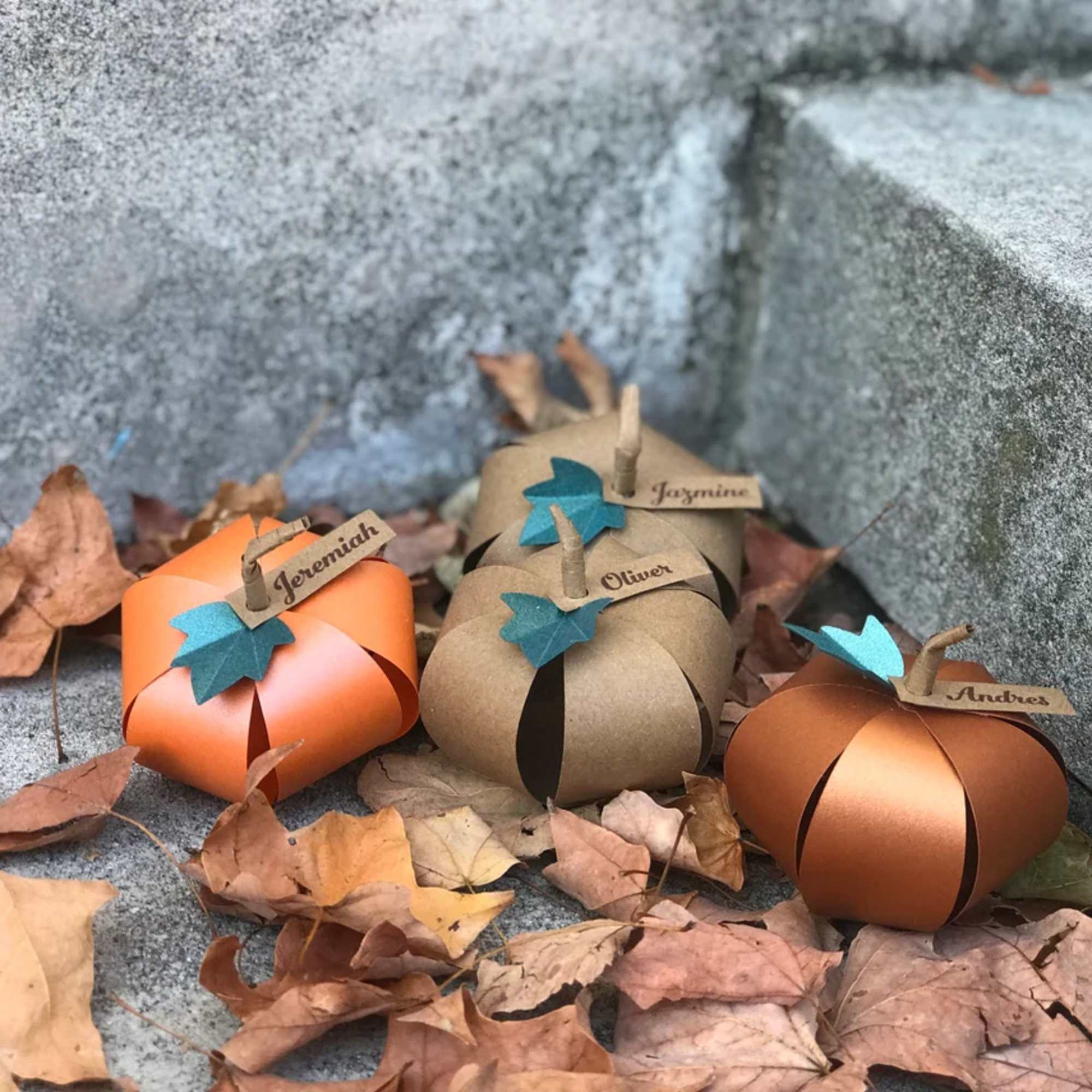 Paper pumpkin place cards on stone steps with autumn leaves