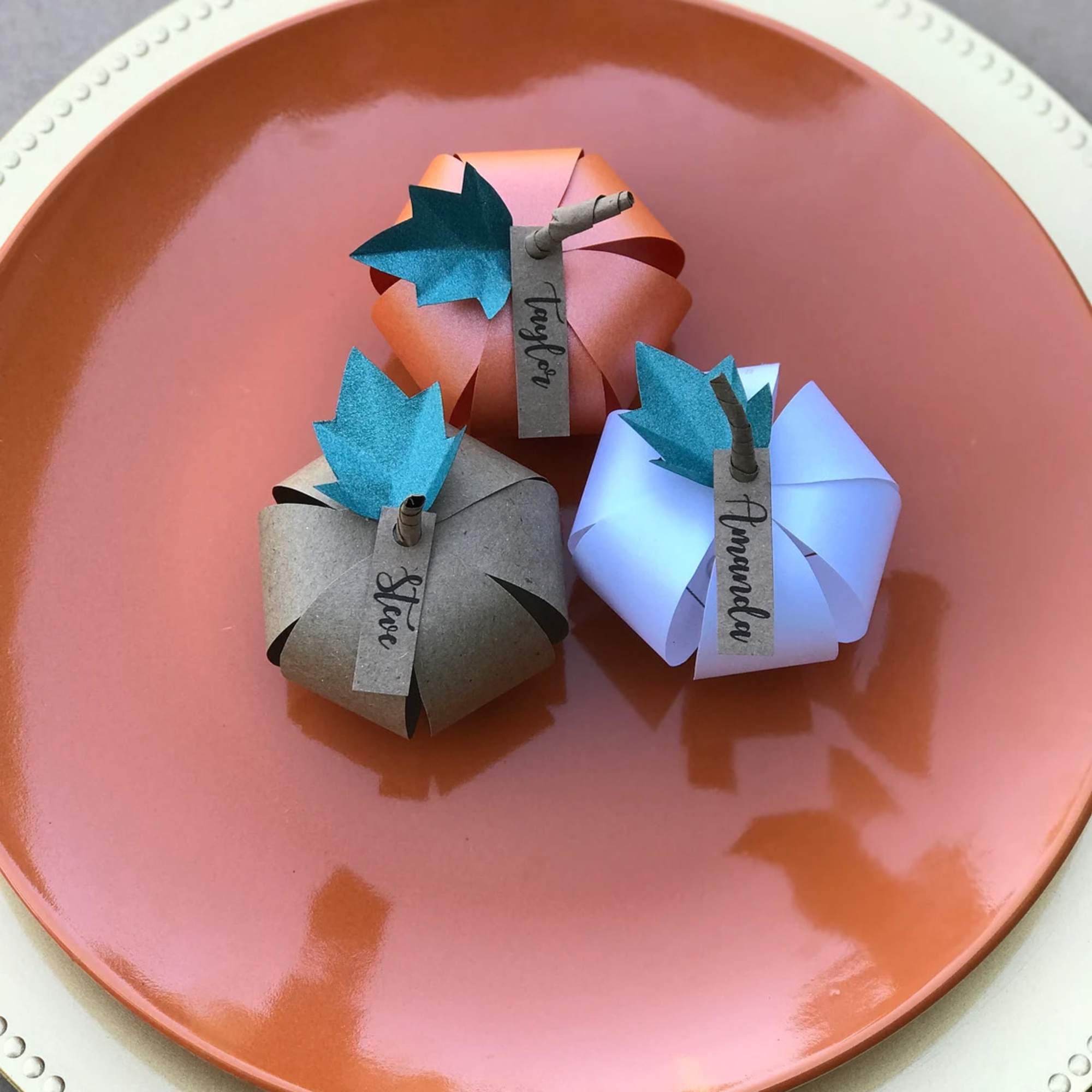 Three folded paper place cards on a round orange plate