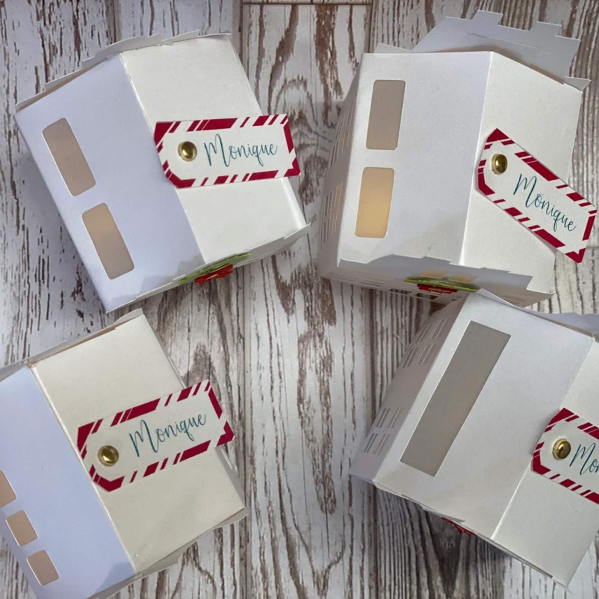 Four small white favor boxes with name tags on a wood surface.
