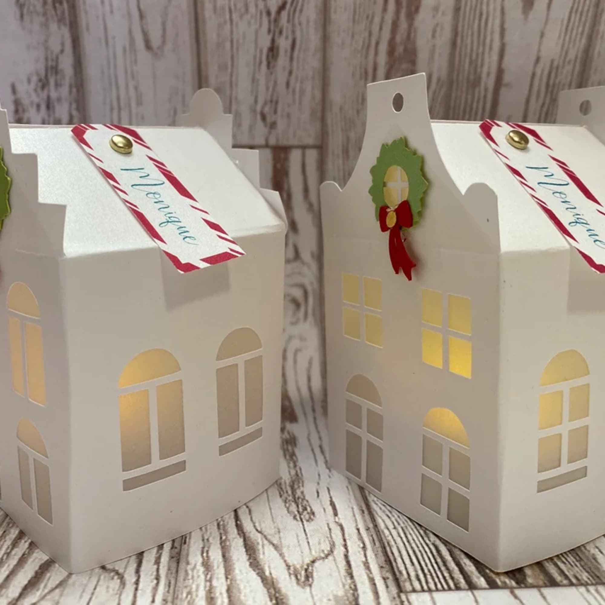 Two white house-shaped gift boxes with holiday tags and wreath accents