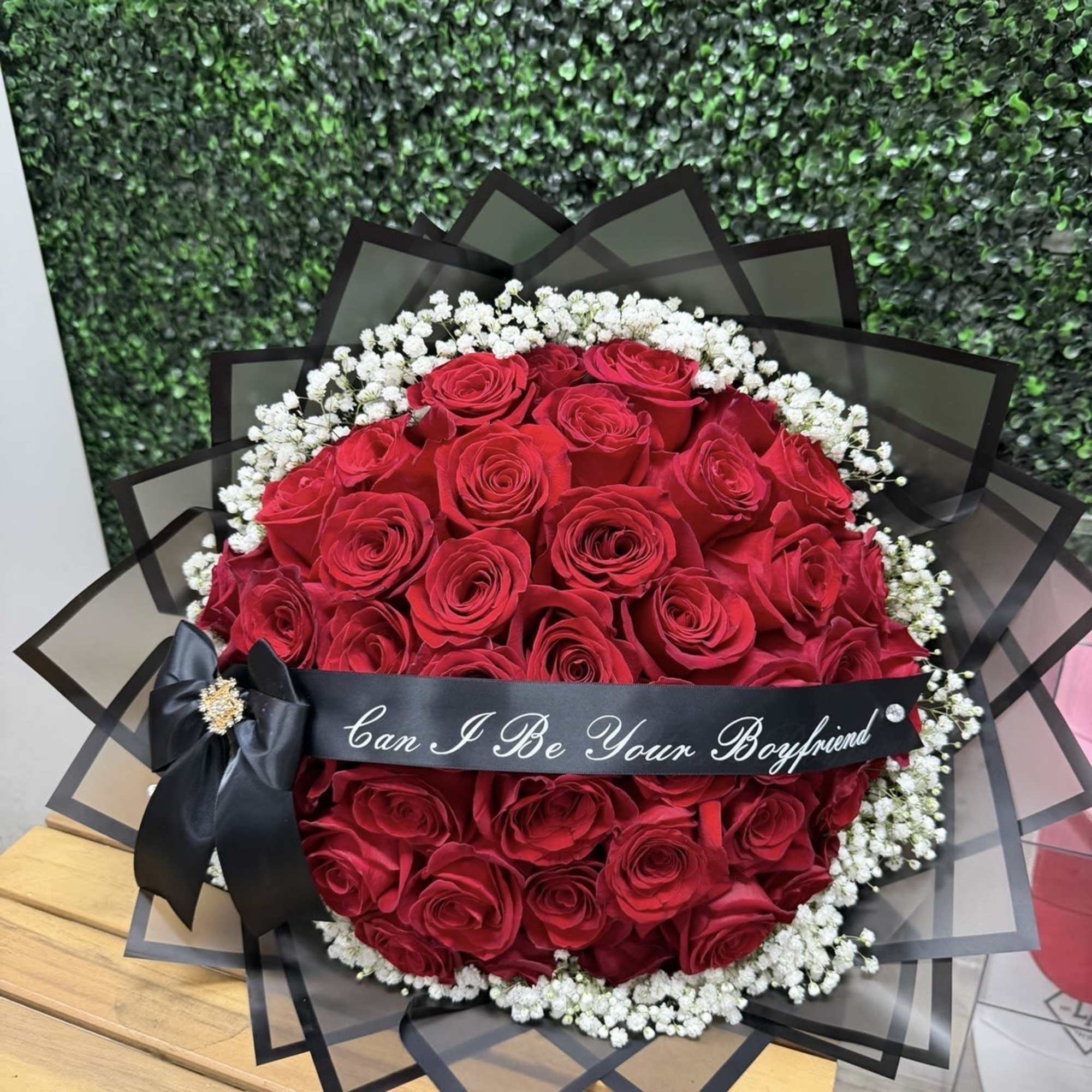 Round bouquet of red roses with white baby's breath and a black ribbon.