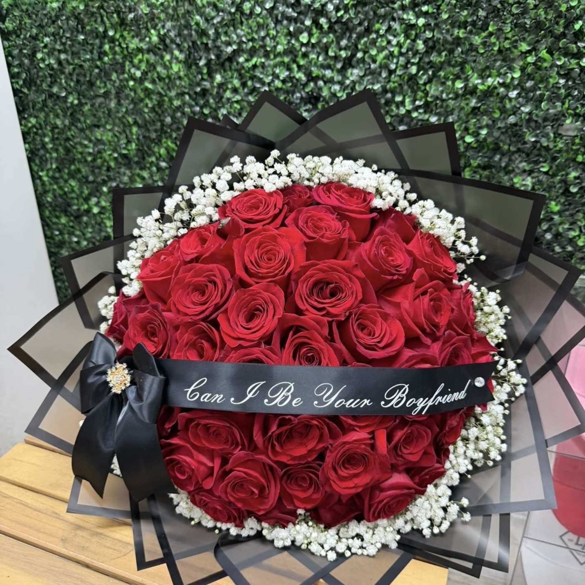 Round bouquet of red roses with white baby's breath and a black ribbon