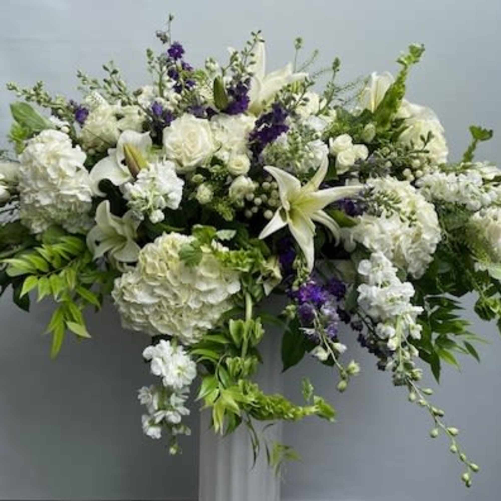 Large white floral arrangement with lilies and roses on a pedestal
