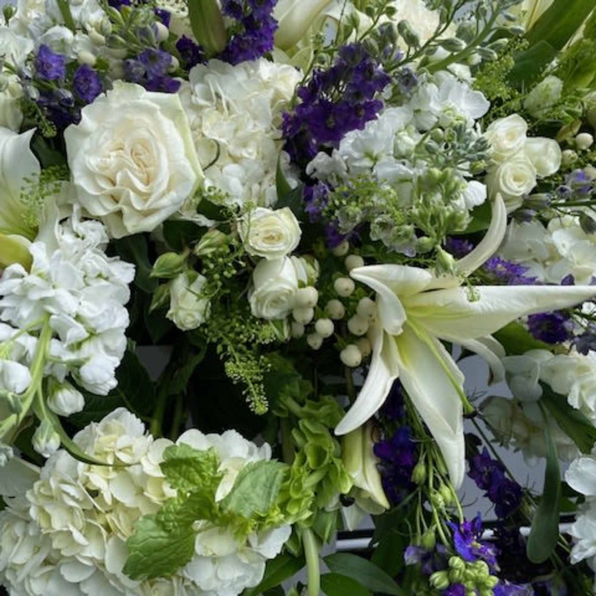 White floral arrangement with lilies, roses, and purple accents