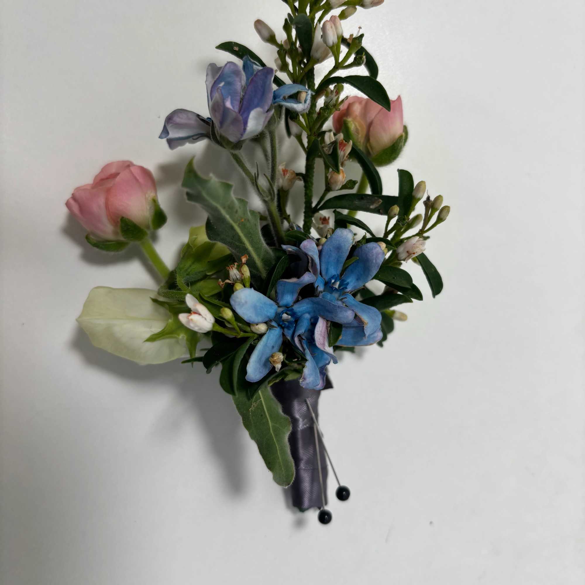 Small boutonniere with blue and pink flowers and a satin ribbon wrap