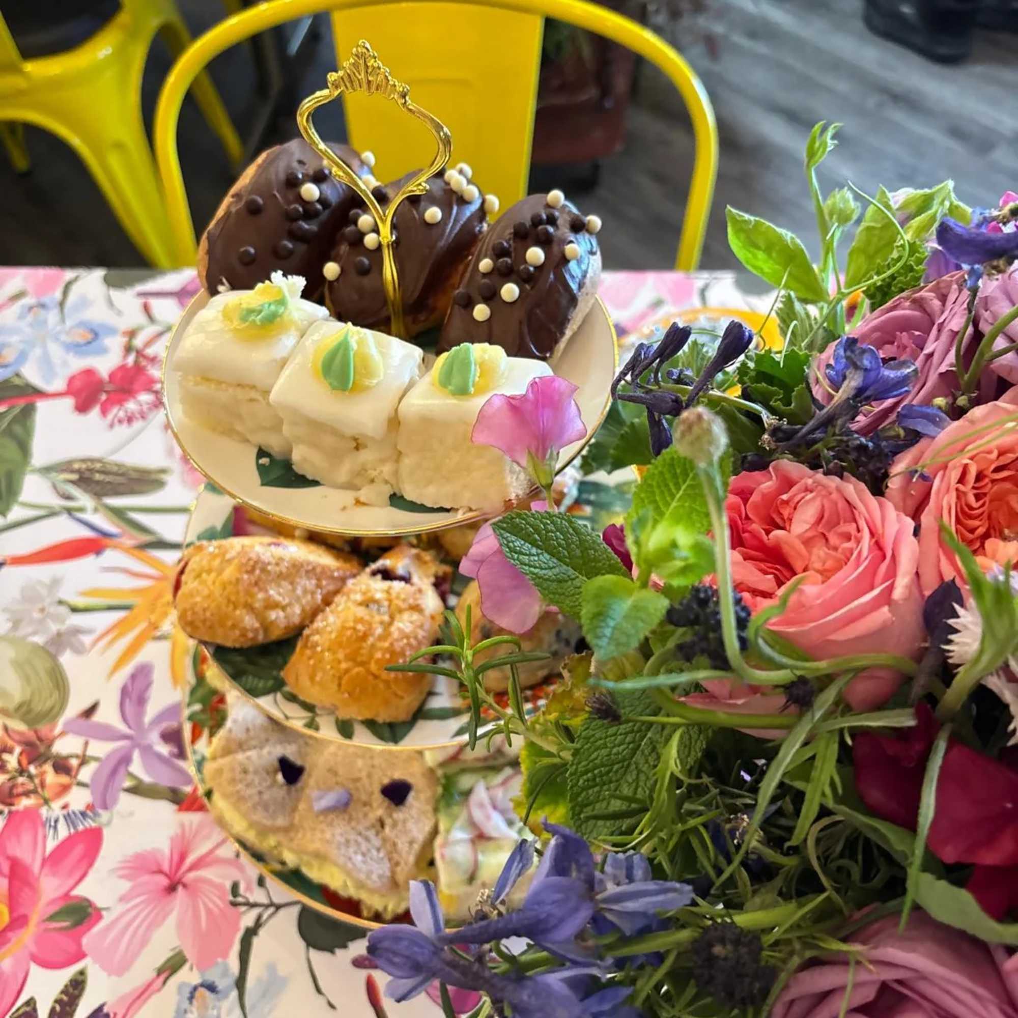 Tiered tray with pastries beside a pink and purple flower arrangement