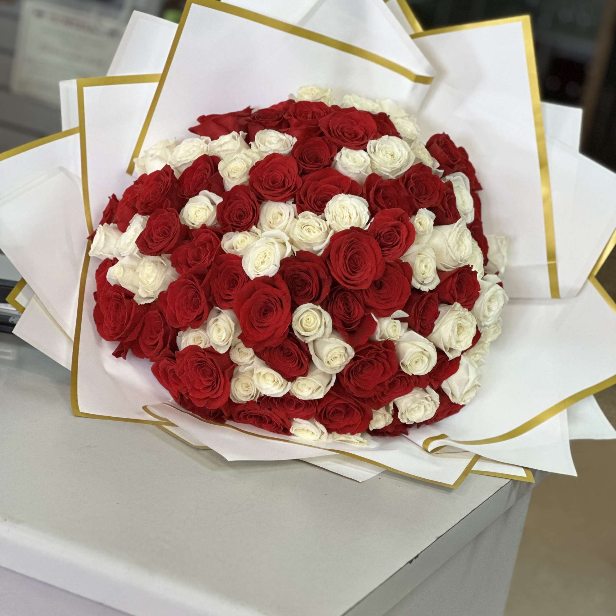 Large bouquet of red and white roses wrapped in white paper with gold trim