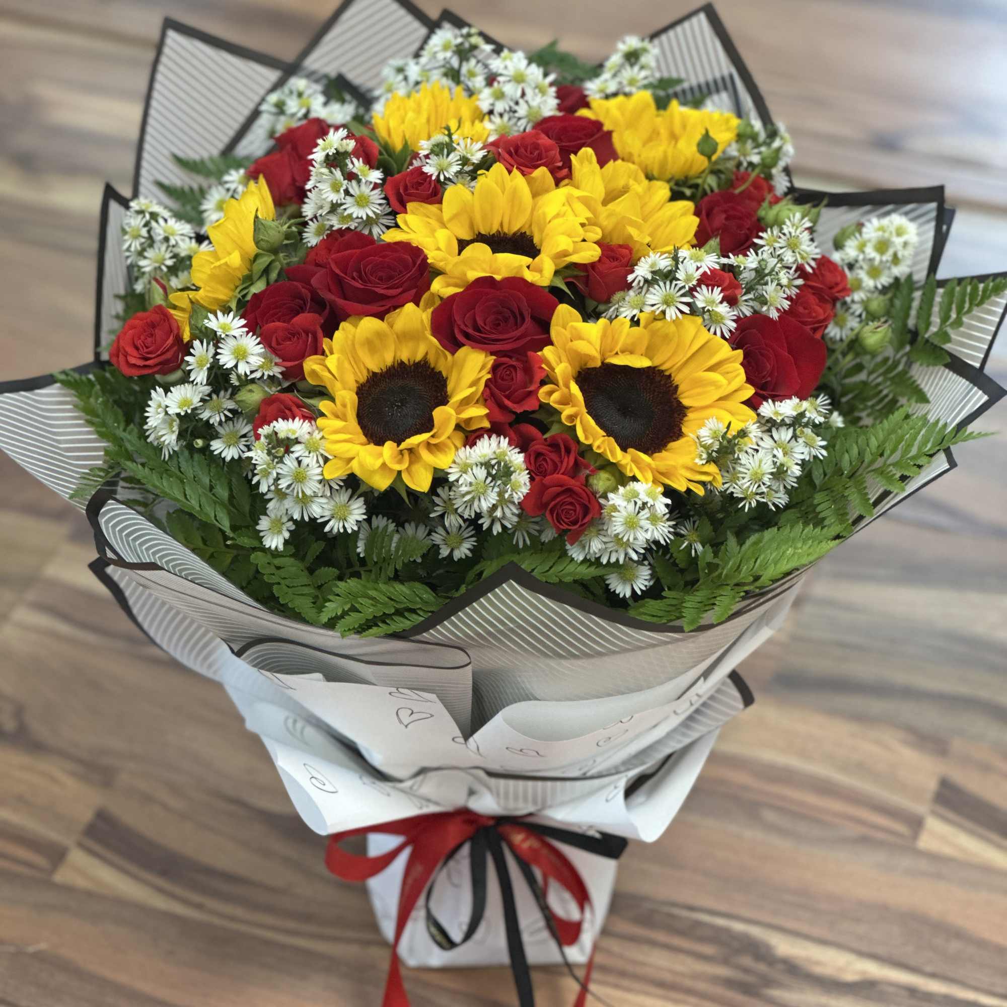 Bouquet of red roses, yellow sunflowers, and white filler flowers wrapped in paper