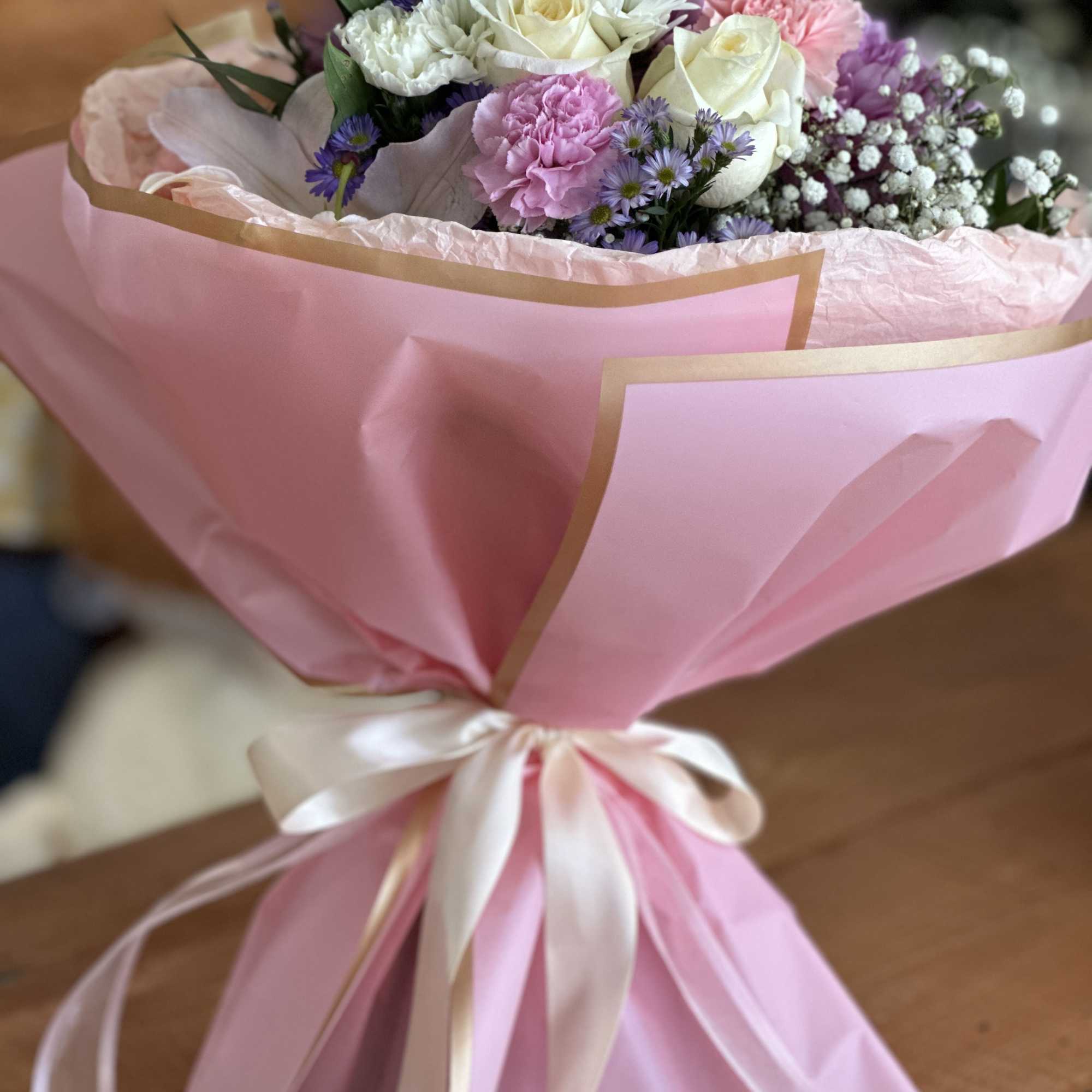 Pink-wrapped bouquet of white and pink flowers with a satin ribbon