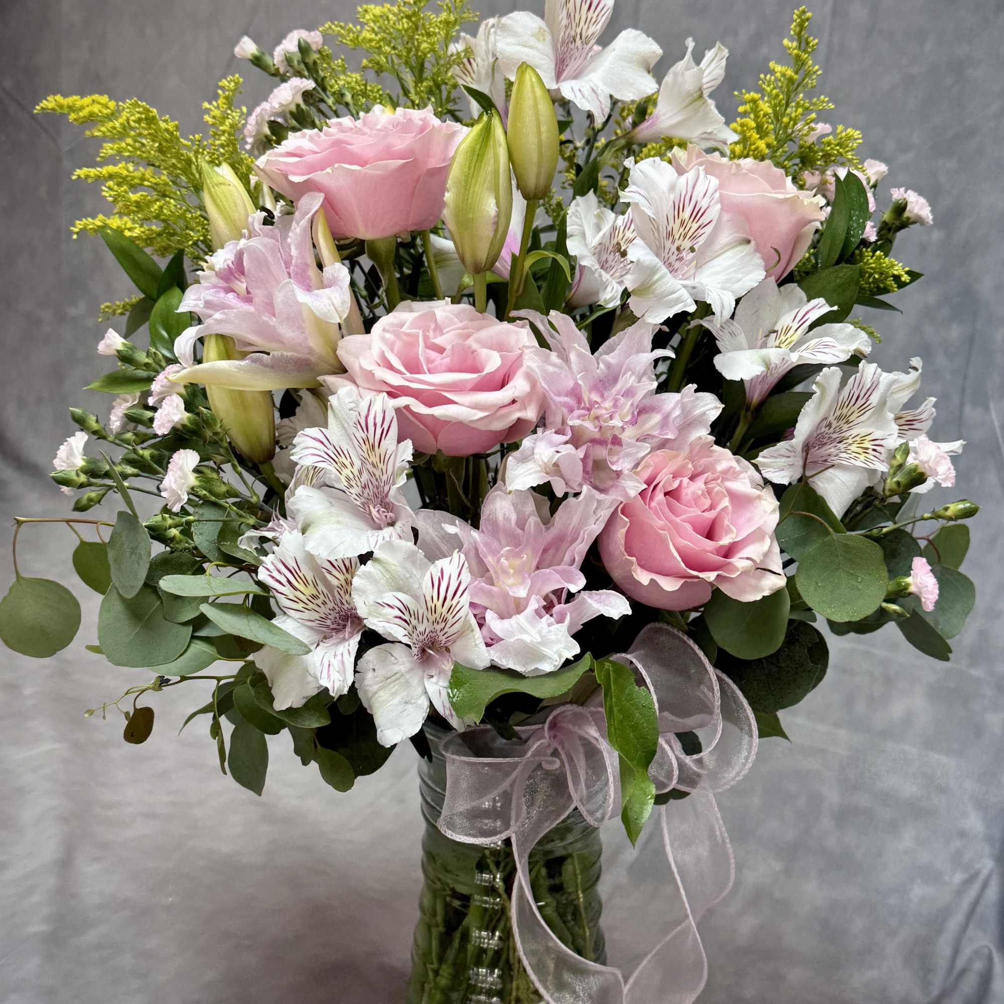 Pink roses and white lilies in a glass vase with a ribbon