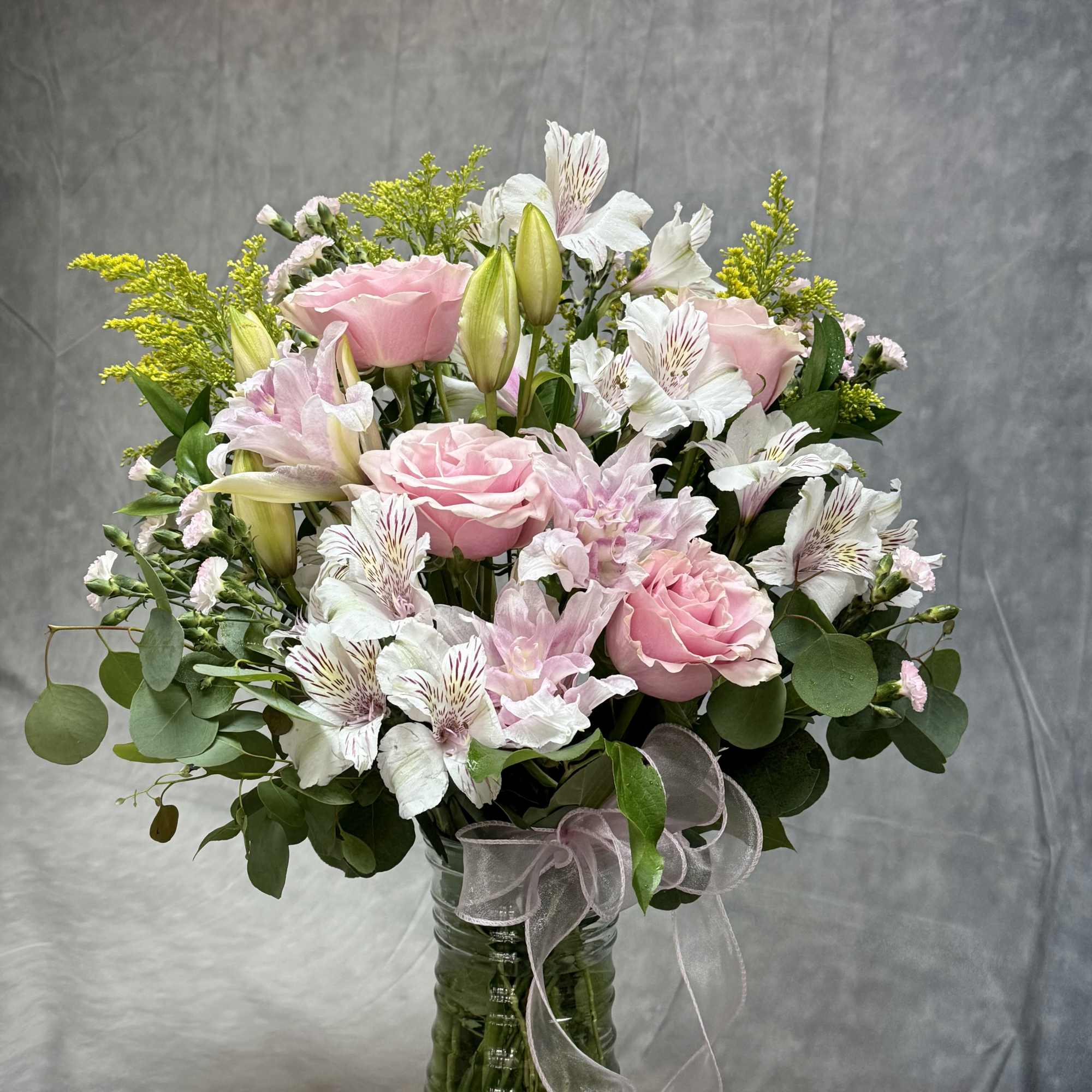Pink roses and white alstroemeria in a glass vase with a ribbon