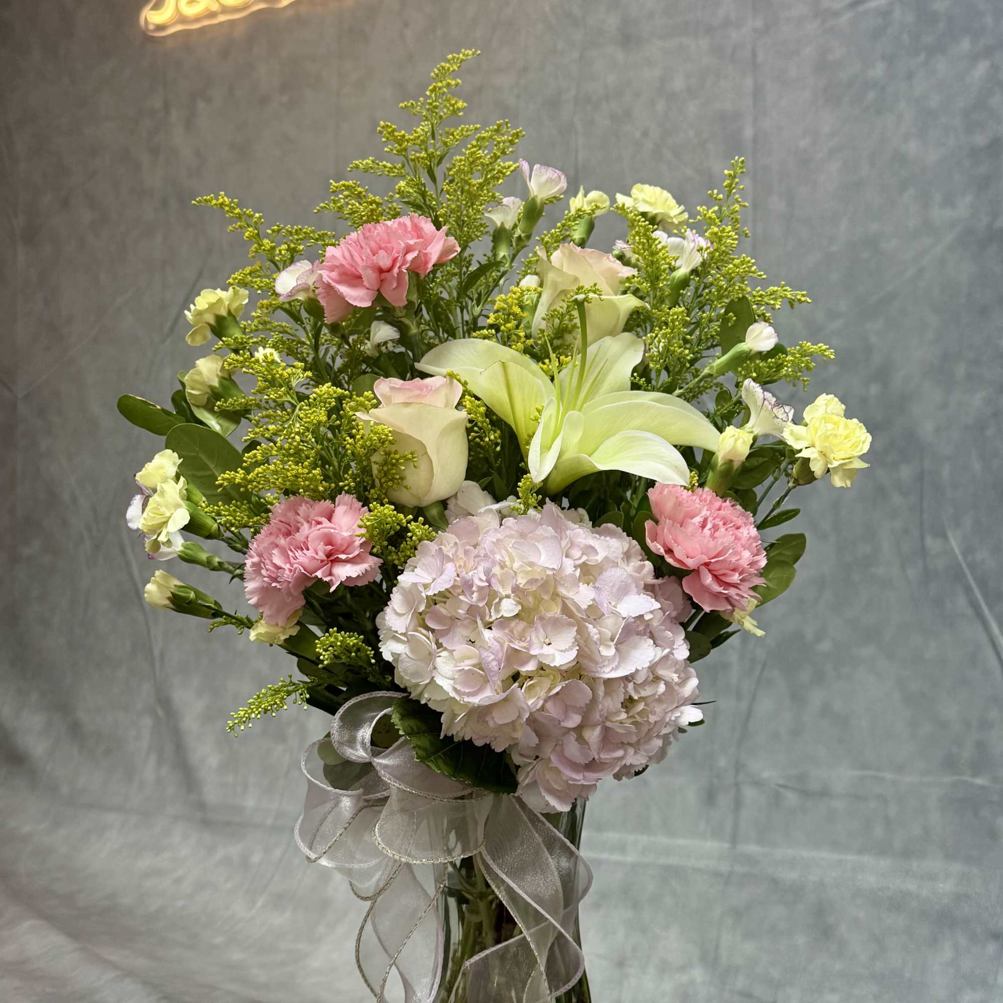Pink and white bouquet with lilies, hydrangea, and carnations in a glass vase