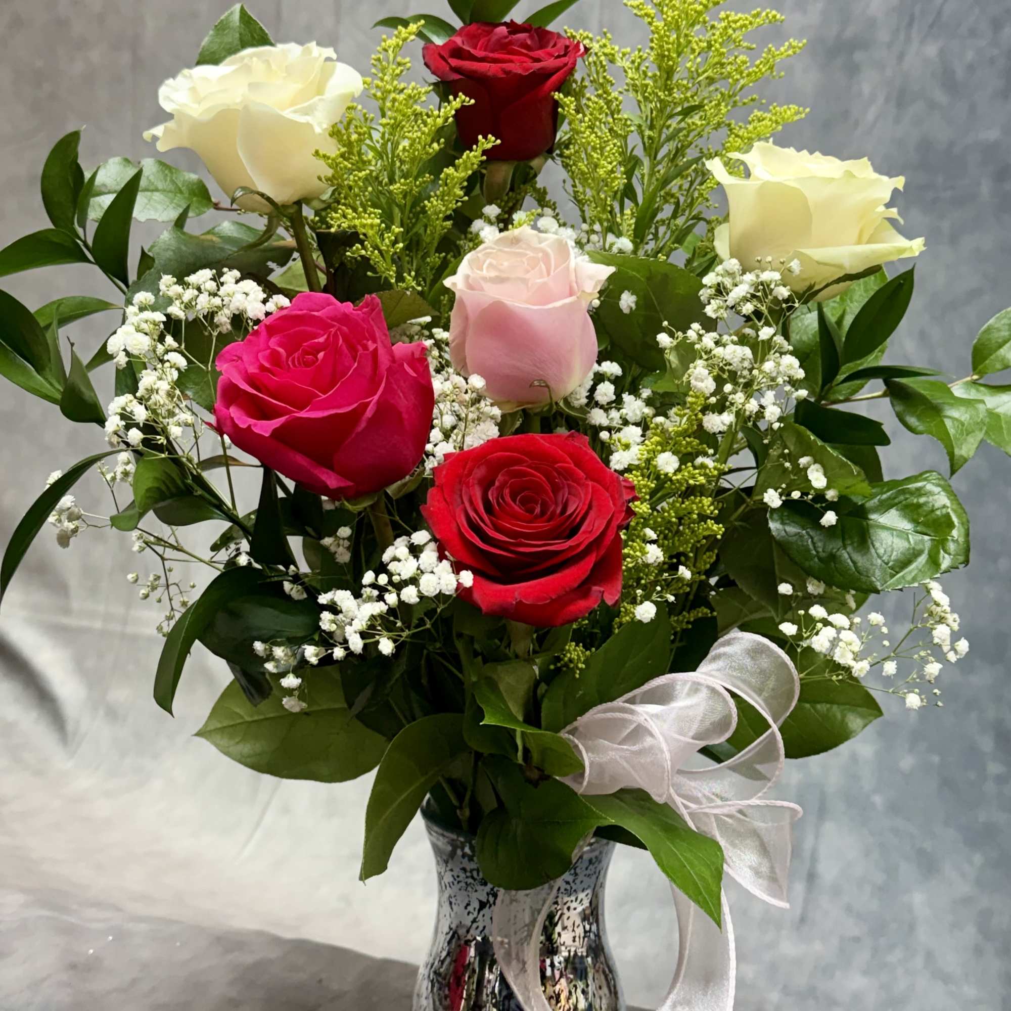 Bouquet of red, pink, and white roses in a silver vase with a white ribbon