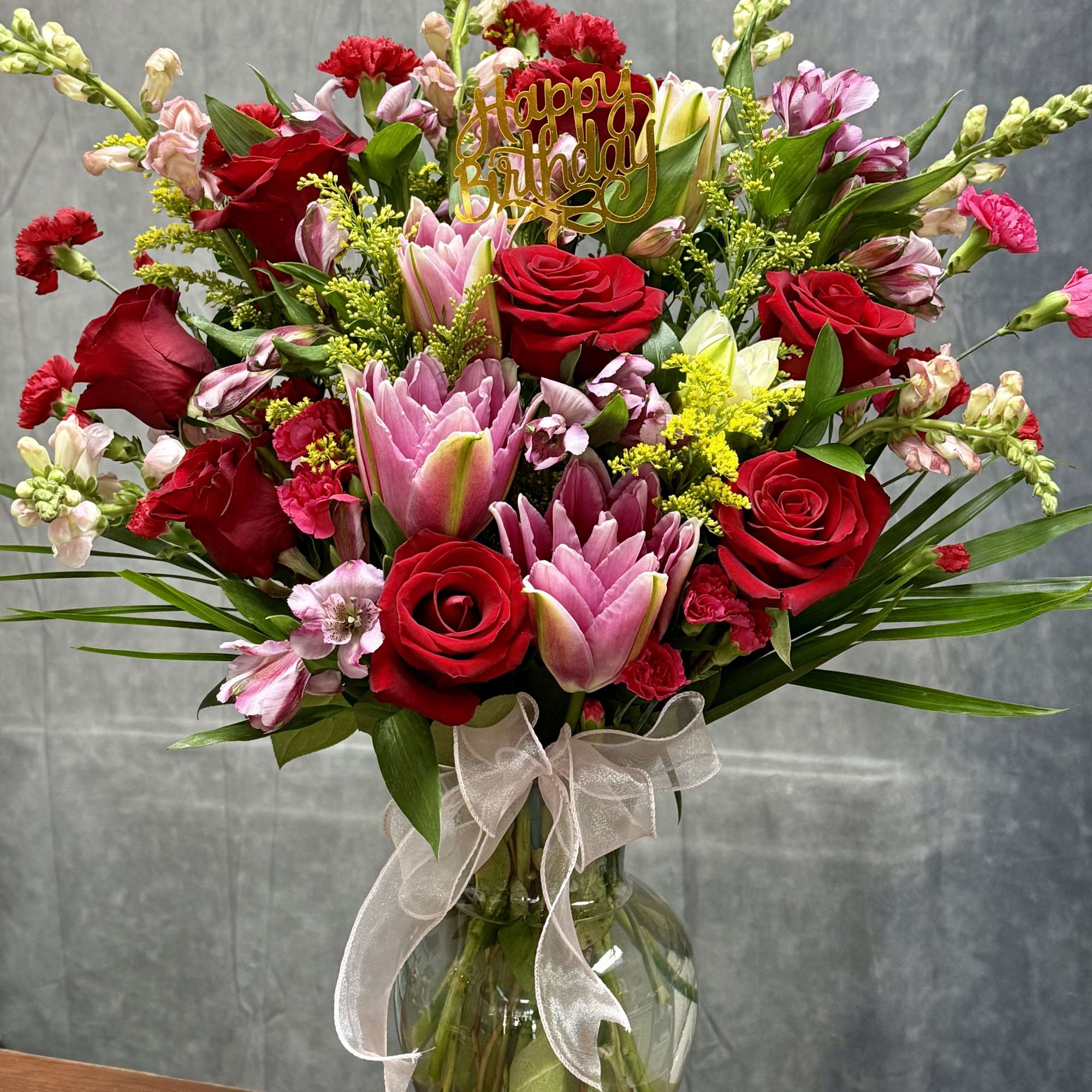 Red roses and pink lilies in a glass vase with a birthday topper