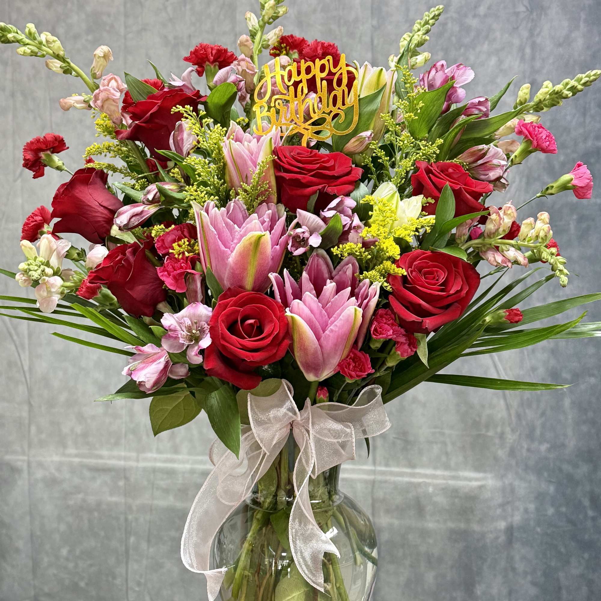 Bouquet of red roses and pink lilies in a glass vase with a birthday topper