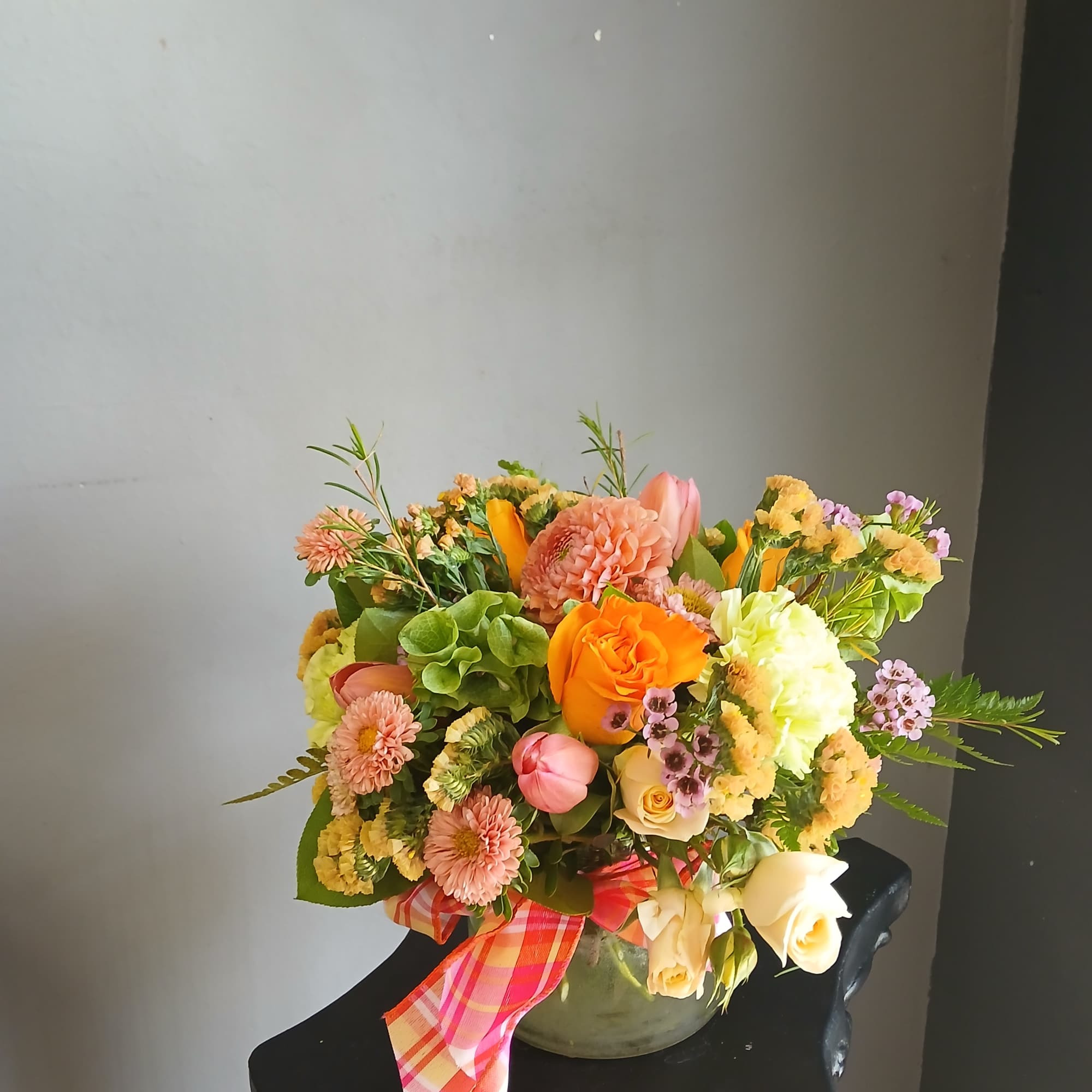 Mixed bouquet of orange, pink, and cream flowers in a vase with a plaid ribbon