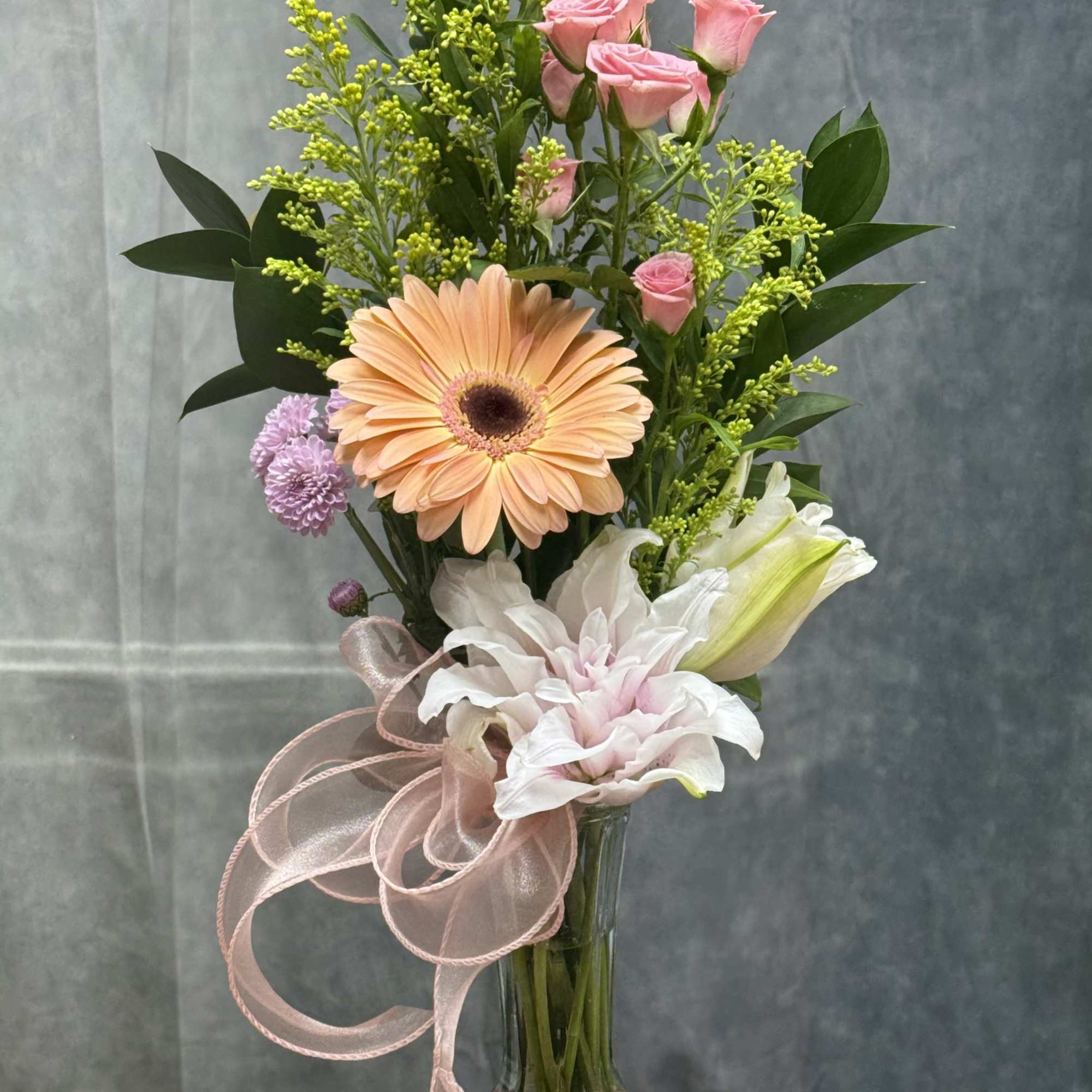 Mixed bouquet in a glass vase with pink roses, a peach gerbera, and white lilies
