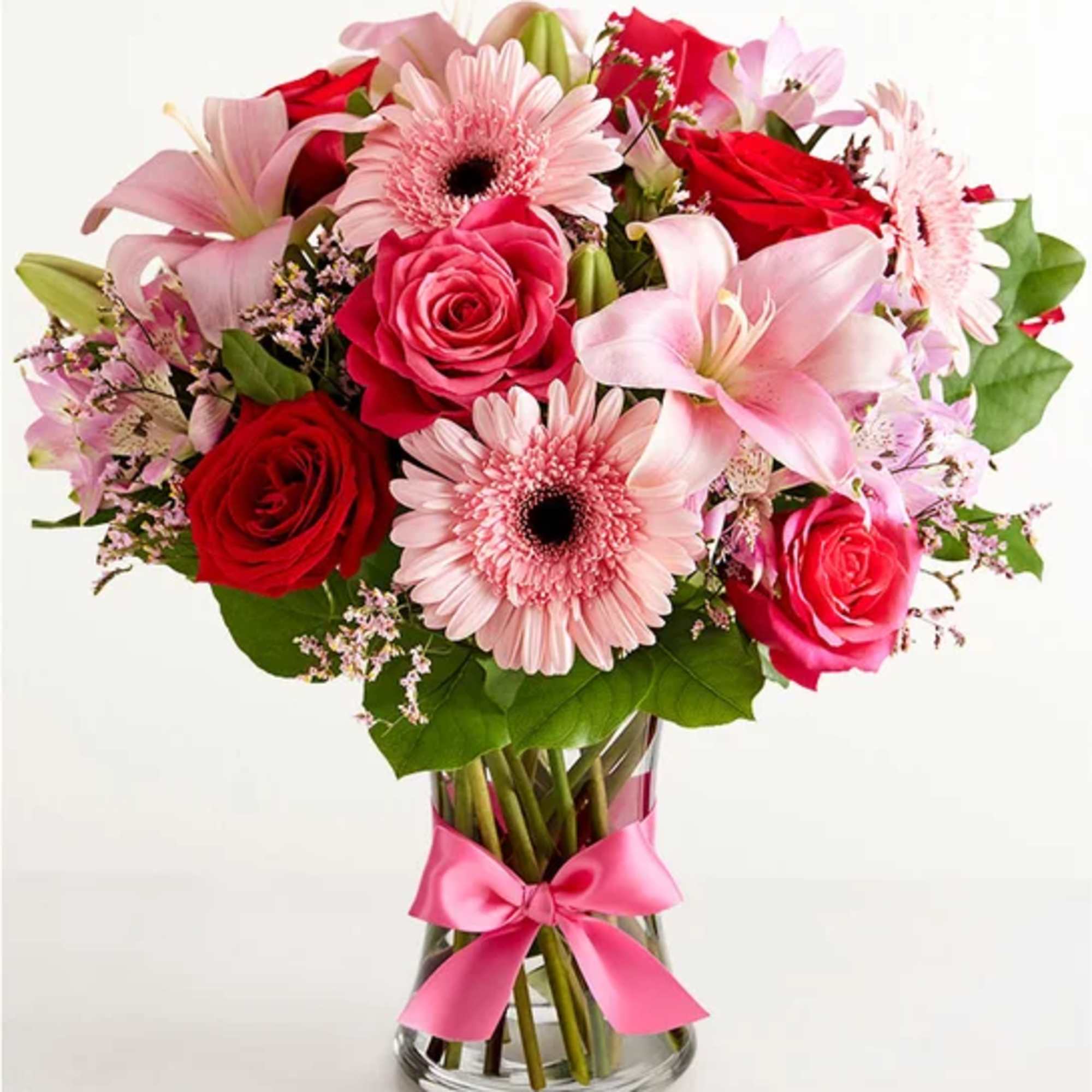 Bouquet of pink lilies, red roses, and pink gerbera daisies in a glass vase